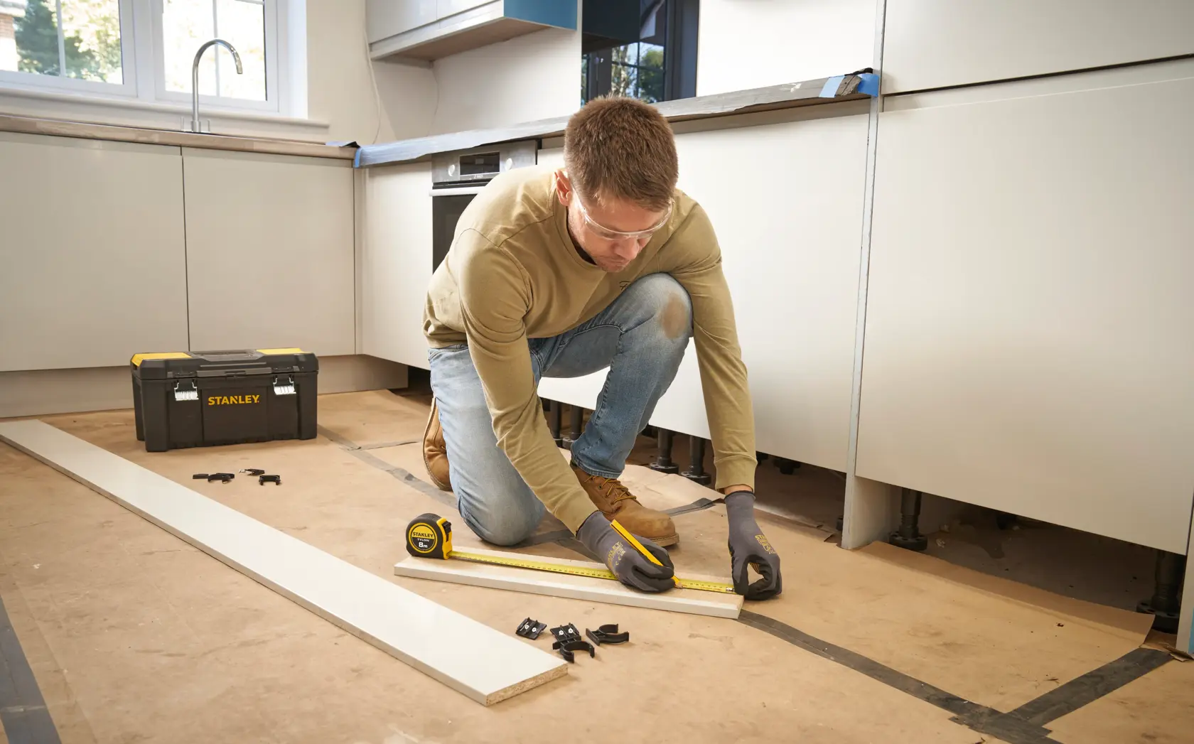 STANLEY 30-393 tape measure in use, carpenter measuring wood plank in kitchen, STANLEY toolbox nearby.