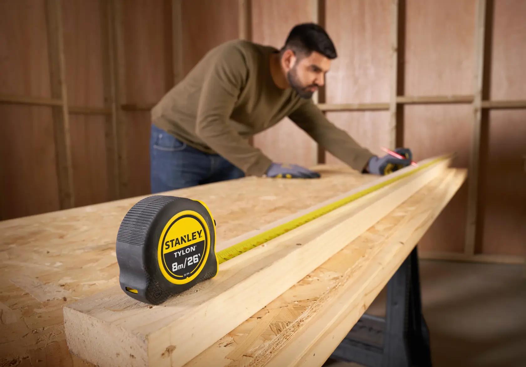 Photo of STANLEY 30-394 tape measure, black and yellow, extended on carpentry table with wood planks.