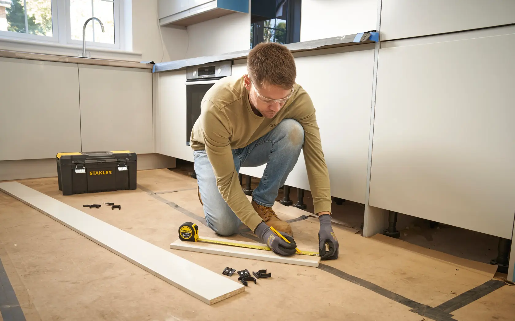 Photo of STANLEY 30-394 tape measure and toolbox in use, person measuring wood in kitchen renovation setting.