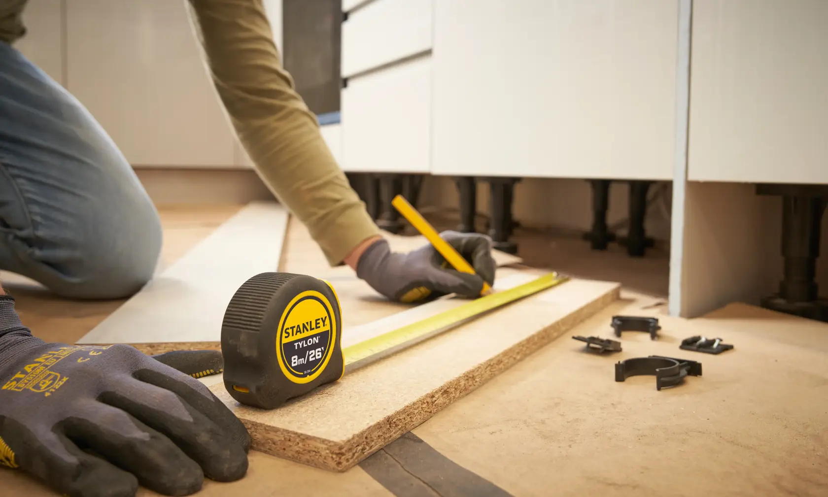 STANLEY 30-394 tape measure on board, worker marking measurement with pencil, close-up view.