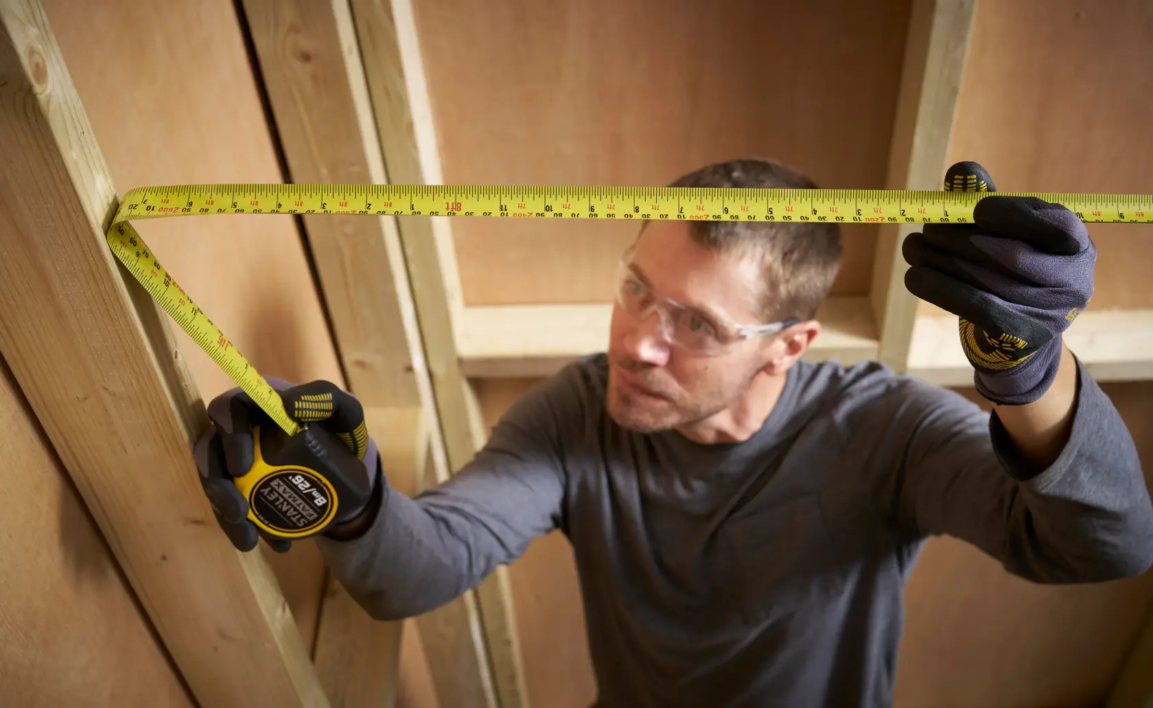 Photo of STANLEY 33-731 tape measure held vertically against wooden studs during construction.