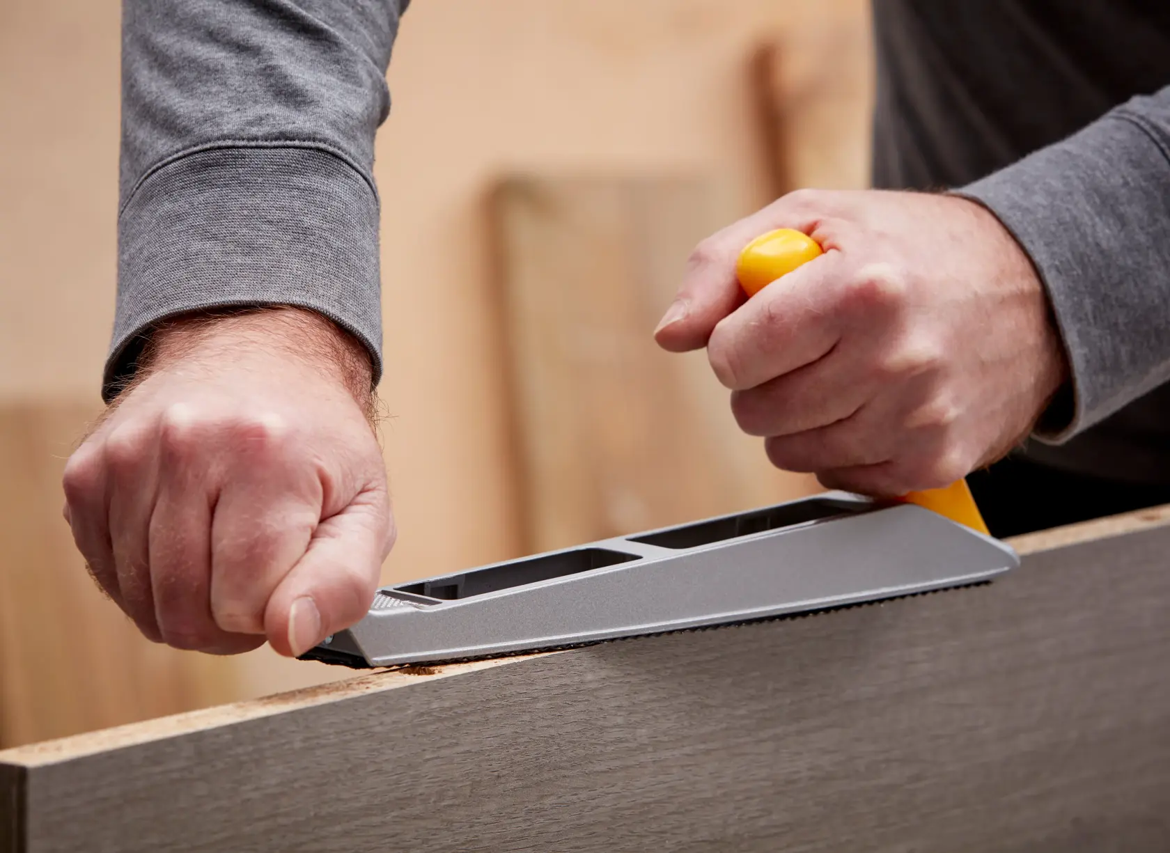 Photo of STANLEY 5-21-122 hand rasp tool shaping the edge of a wooden board, close-up of use in workshop.