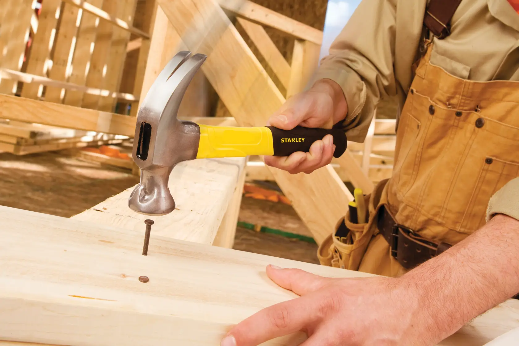 Photo of STANLEY 51-508 claw hammer with yellow handle driving a nail into wood at a construction site.