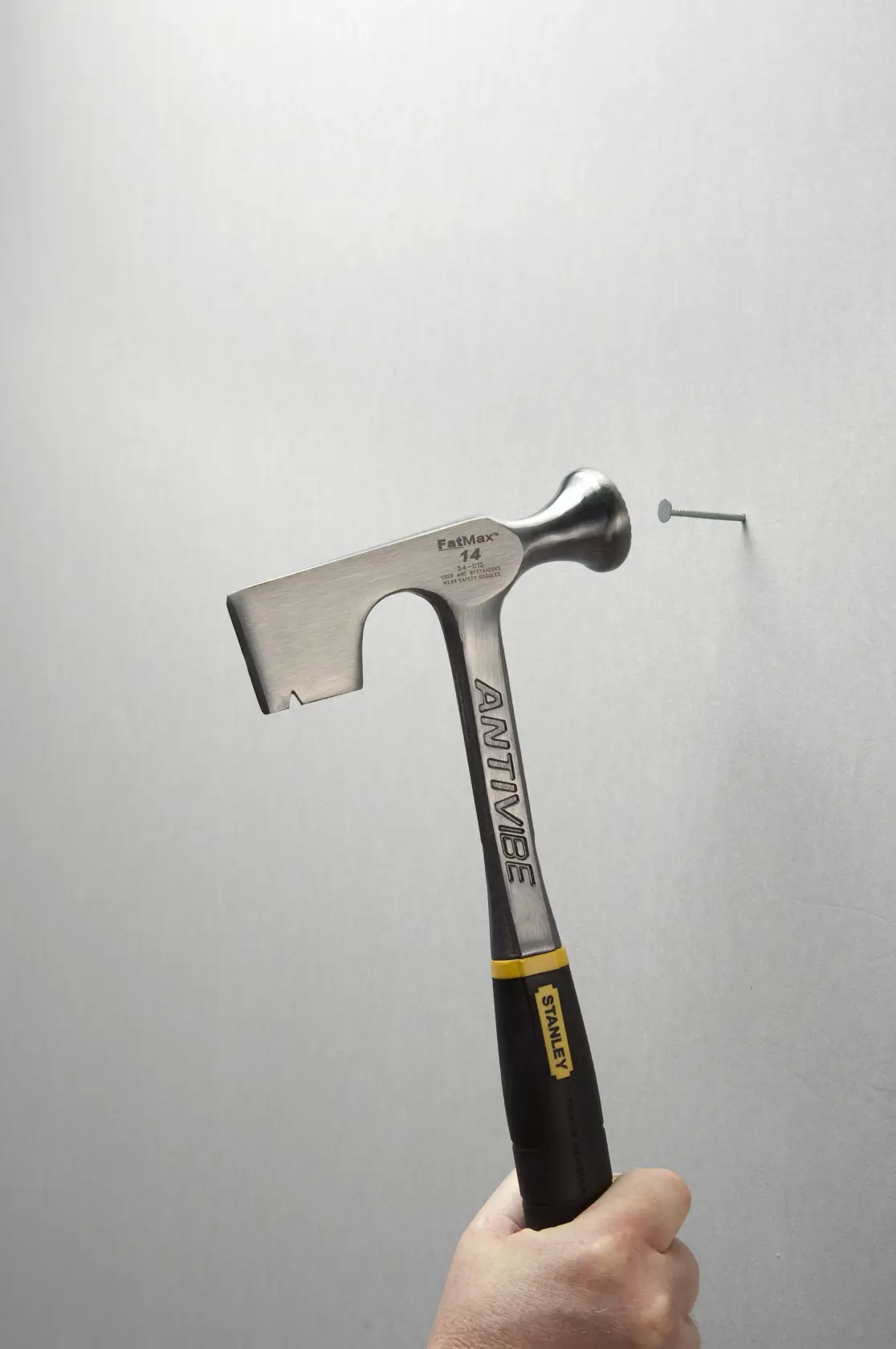 Stanley 54-015 hammer with black and yellow handle, striking a nail on a gray surface, side angle.