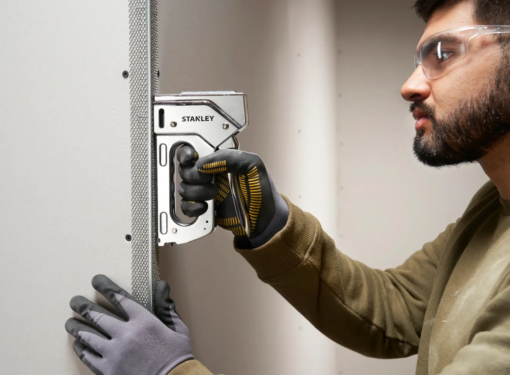 Stanley 6-TR110 heavy-duty staple gun used on drywall, close-up of gloved hands during construction task.