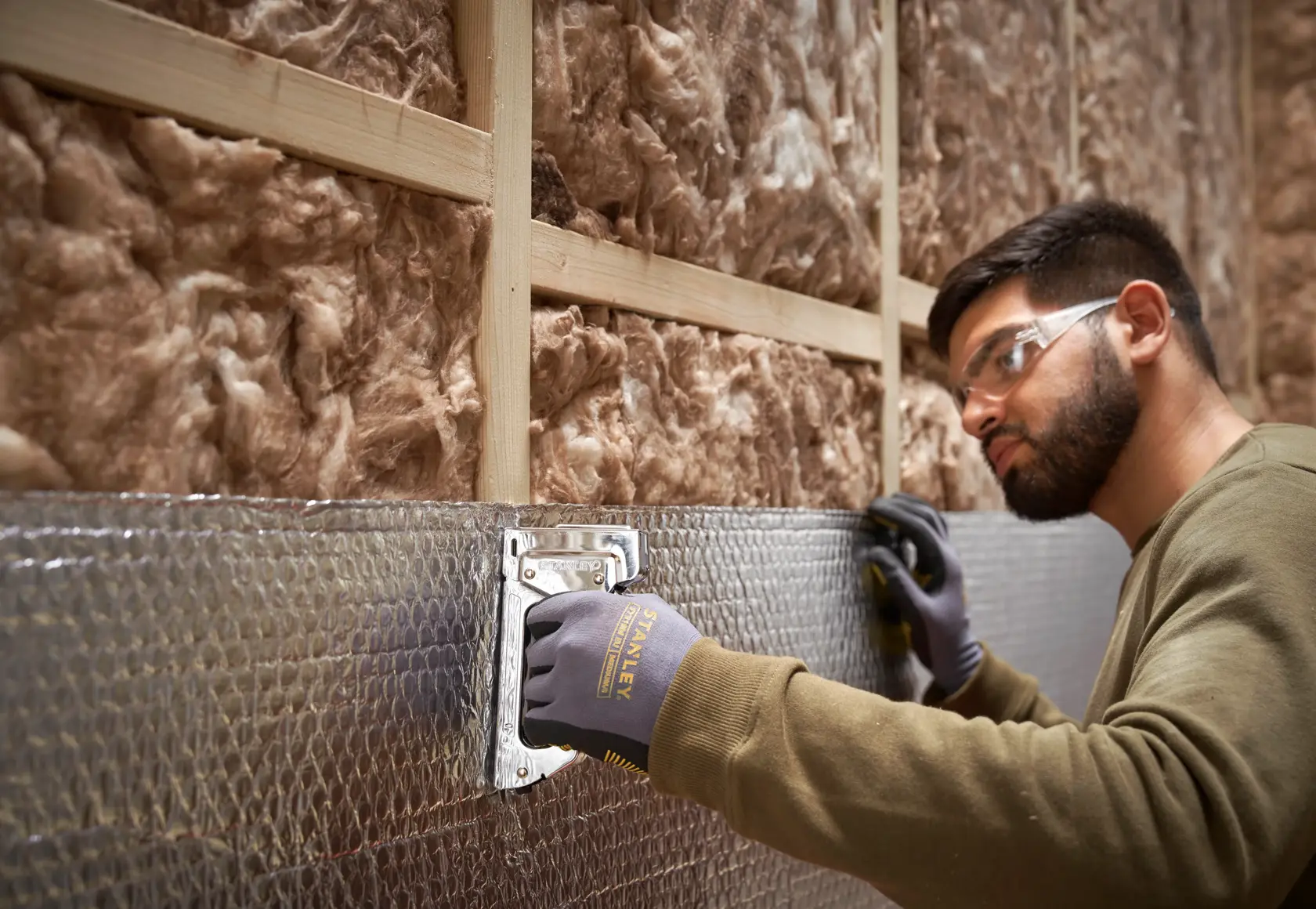 Photo of STANLEY 6-TR45 staple gun being used to attach insulation to a wall, close-up of hand and tool.