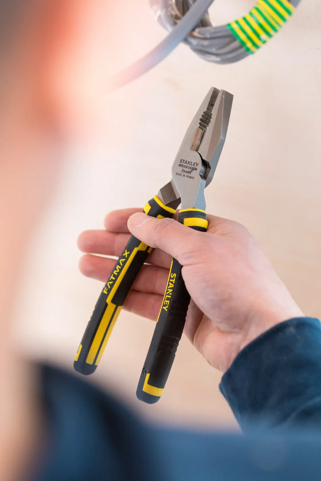 Photo of STANLEY 89-868 pliers with black and yellow handles, held in hand near electrical wire.