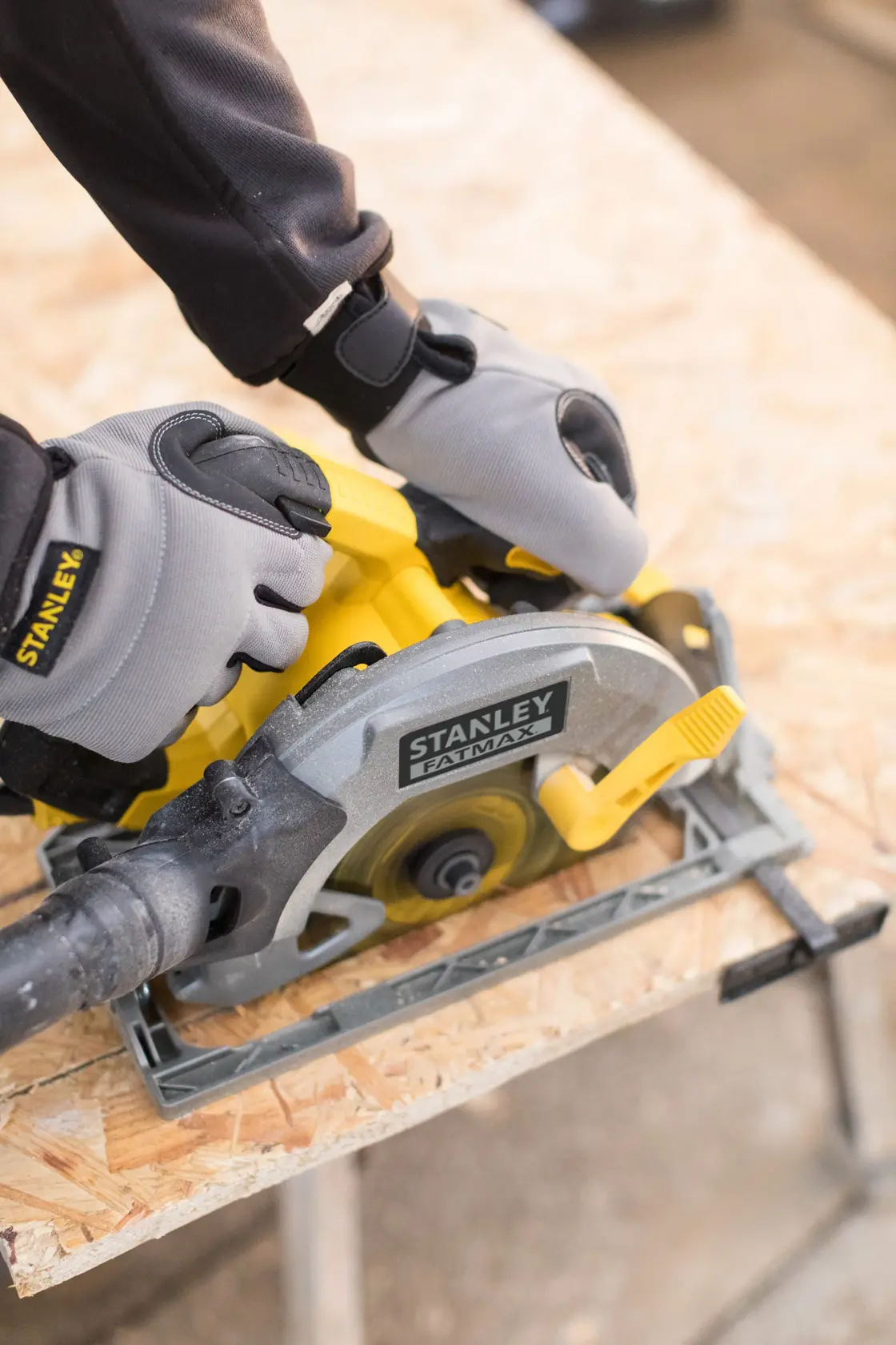 STANLEY FME301 circular saw in use, photographed from above, with gloved hands cutting plywood.
