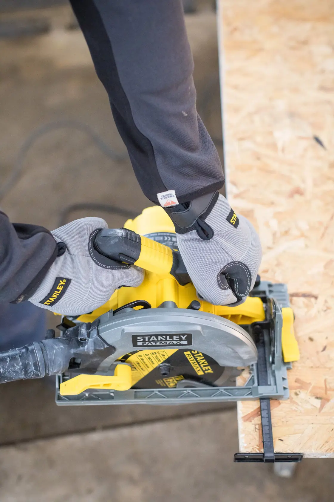 STANLEY FME301 circular saw cutting plywood, worker hands in gloves holding tool, top view.