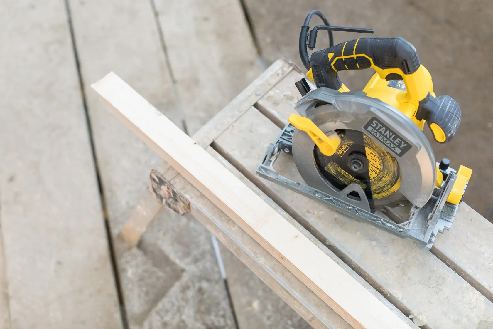 Photo of STANLEY FME301 circular saw, yellow and black, on a workbench next to a wooden plank, top view.