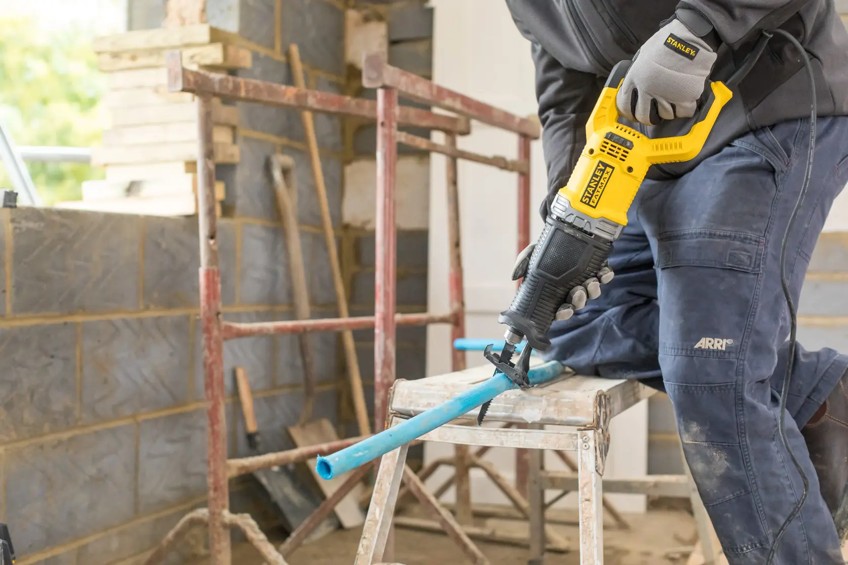 STANLEY FME360 reciprocating saw in use cutting a blue pipe at a construction site, angled side view.