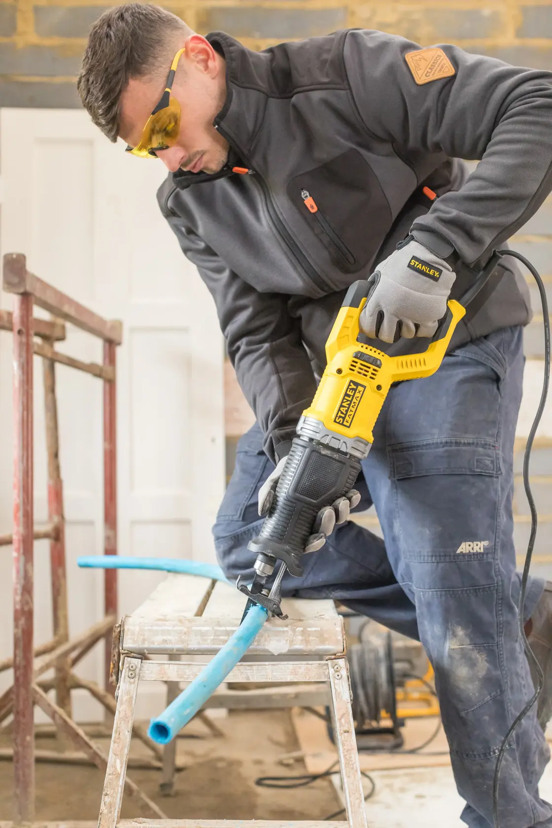 STANLEY FME360 reciprocating saw cutting blue pipe on workbench in workshop.