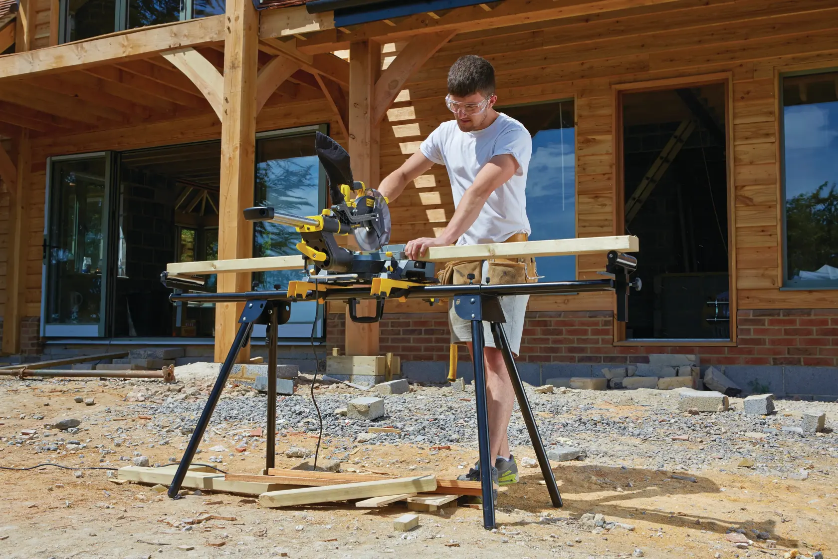 STANLEY FME790-XE mitre saw on stand, used outdoors by person cutting wood, construction site background.