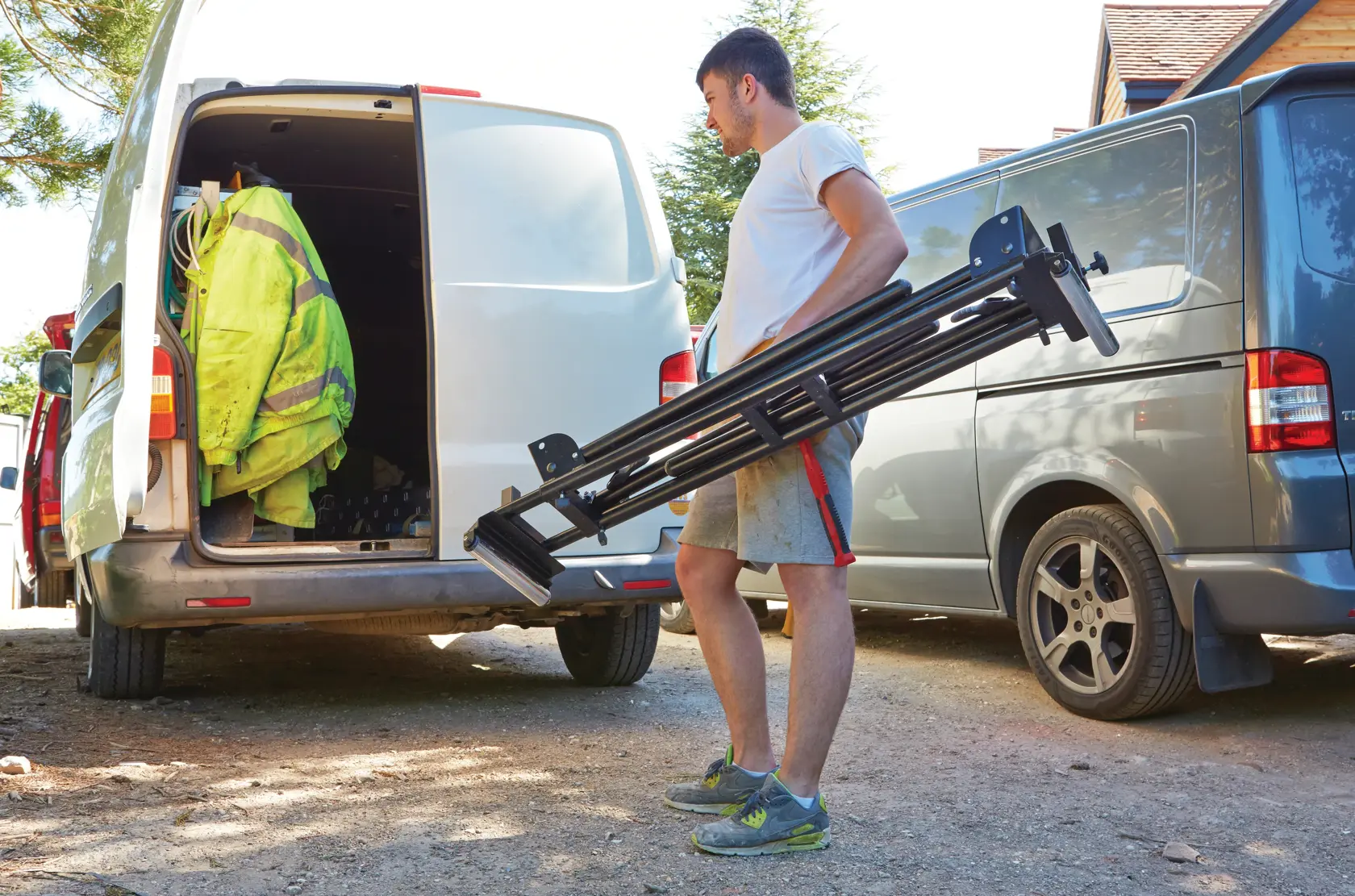 STANLEY FME790-XE photography tripod carried by a person near two parked vans outdoors.