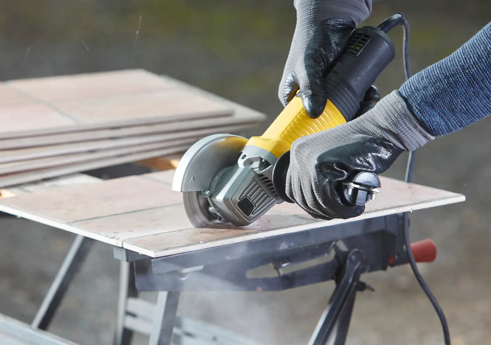 STANLEY FMEG220 angle grinder cutting tile, close-up, black and yellow tool held by gloved hands.