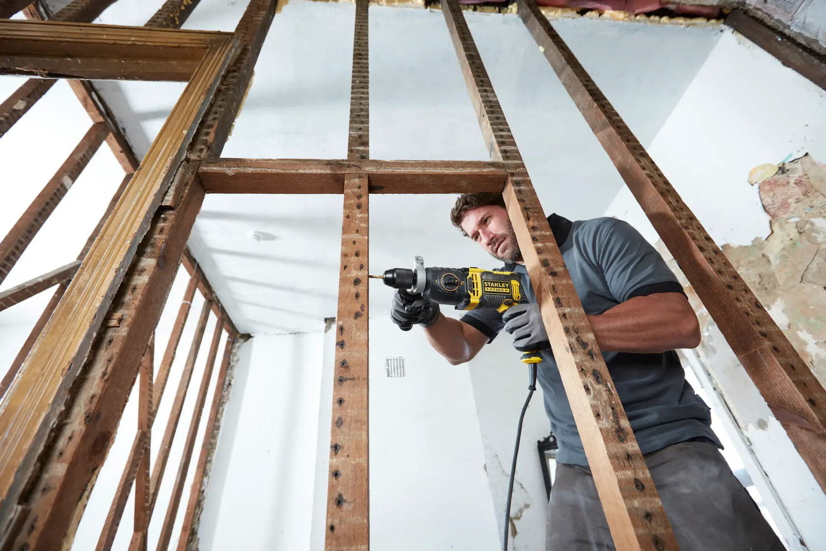 Photo of STANLEY FMEH1100K hammer drill in use on wooden framing, construction setting, side angle.