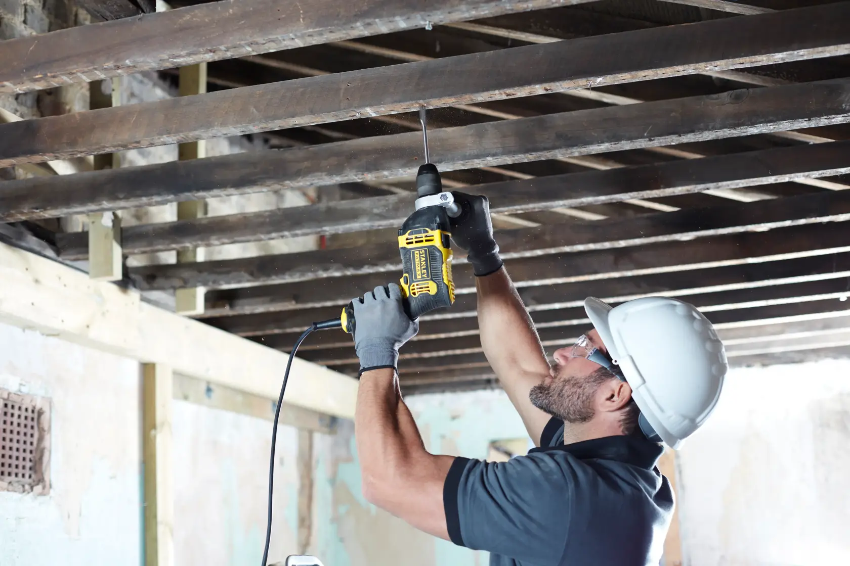 STANLEY FMEH750 corded drill being used overhead by worker with gloves and helmet in construction setting.