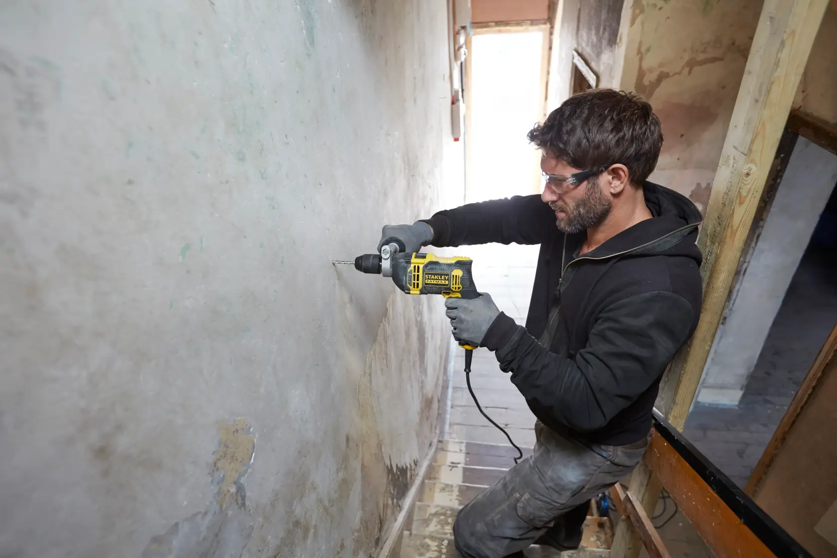 Person using STANLEY FMEH750 corded drill on wall in a construction area, side angle.