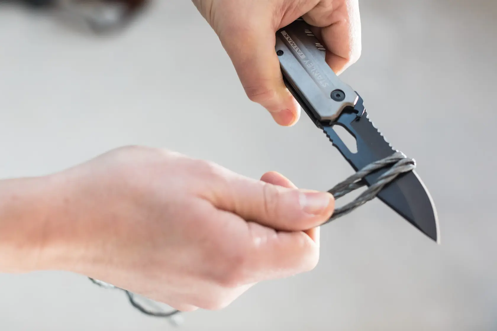 STANLEY FMHT0-10312 folding knife cutting wire, close-up view of hands using the knife.
