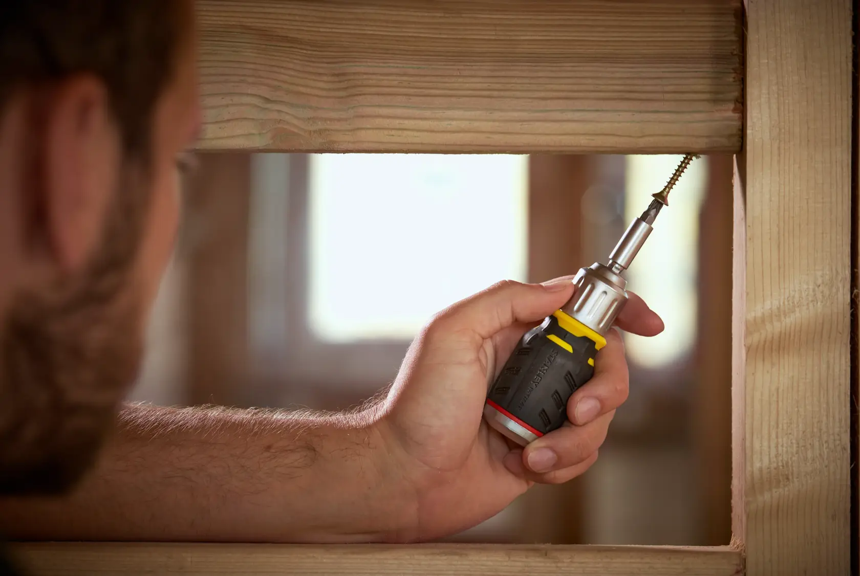 STANLEY FMHT0-62688 screwdriver used to drive screw into wood frame, close-up photo.