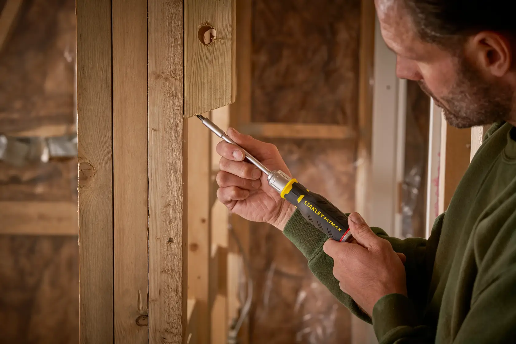 Photo of STANLEY FMHT0-62690 screwdriver used on wooden construction by person in green sweater.