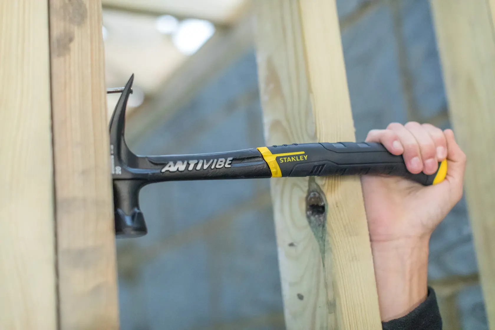 STANLEY FMHT1-51277 claw hammer in use, black handle, driving nail into wooden beams.
