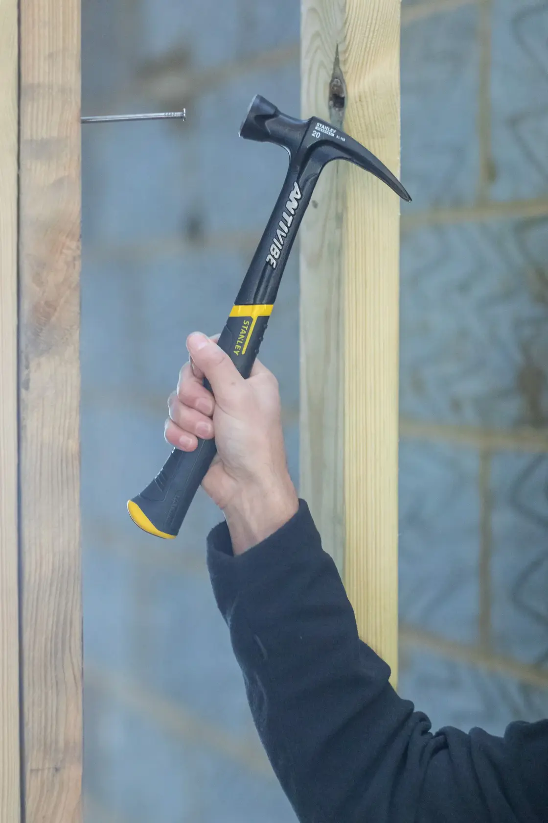 Stanley FMHT1-51277 claw hammer in use, black and yellow handle, construction scene.