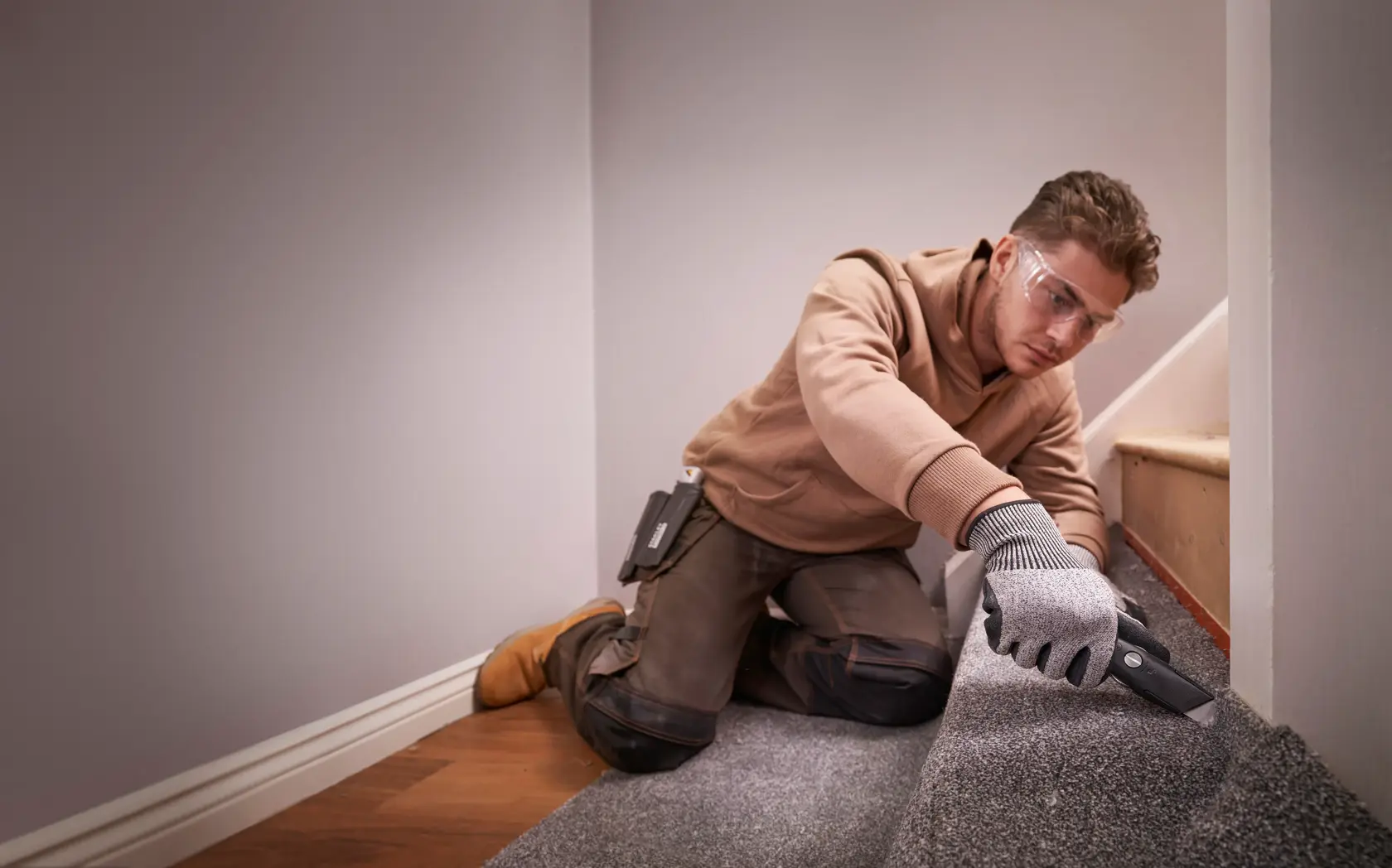 STANLEY FMHT10500-0 utility knife used to cut grey carpet on stairs, indoor setting.