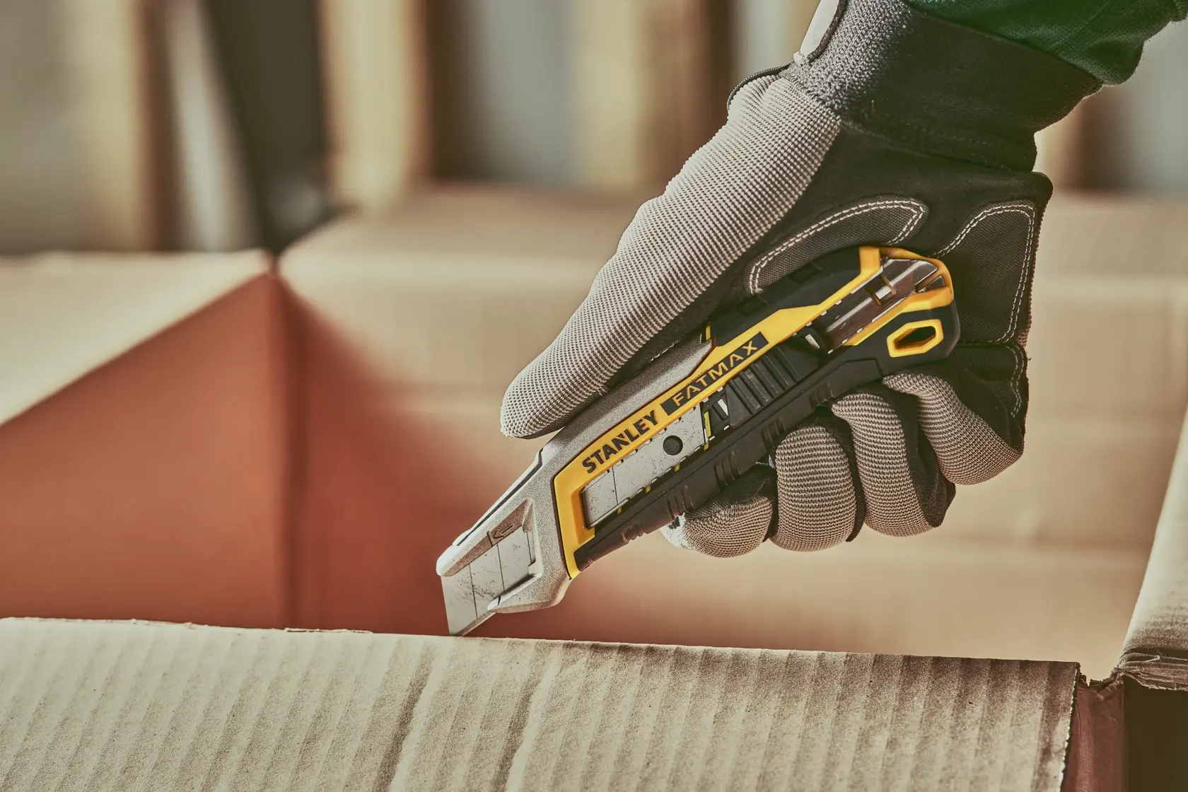 Photo of STANLEY FMHT10594-0 utility knife cutting cardboard box, worker wearing grey protective glove.