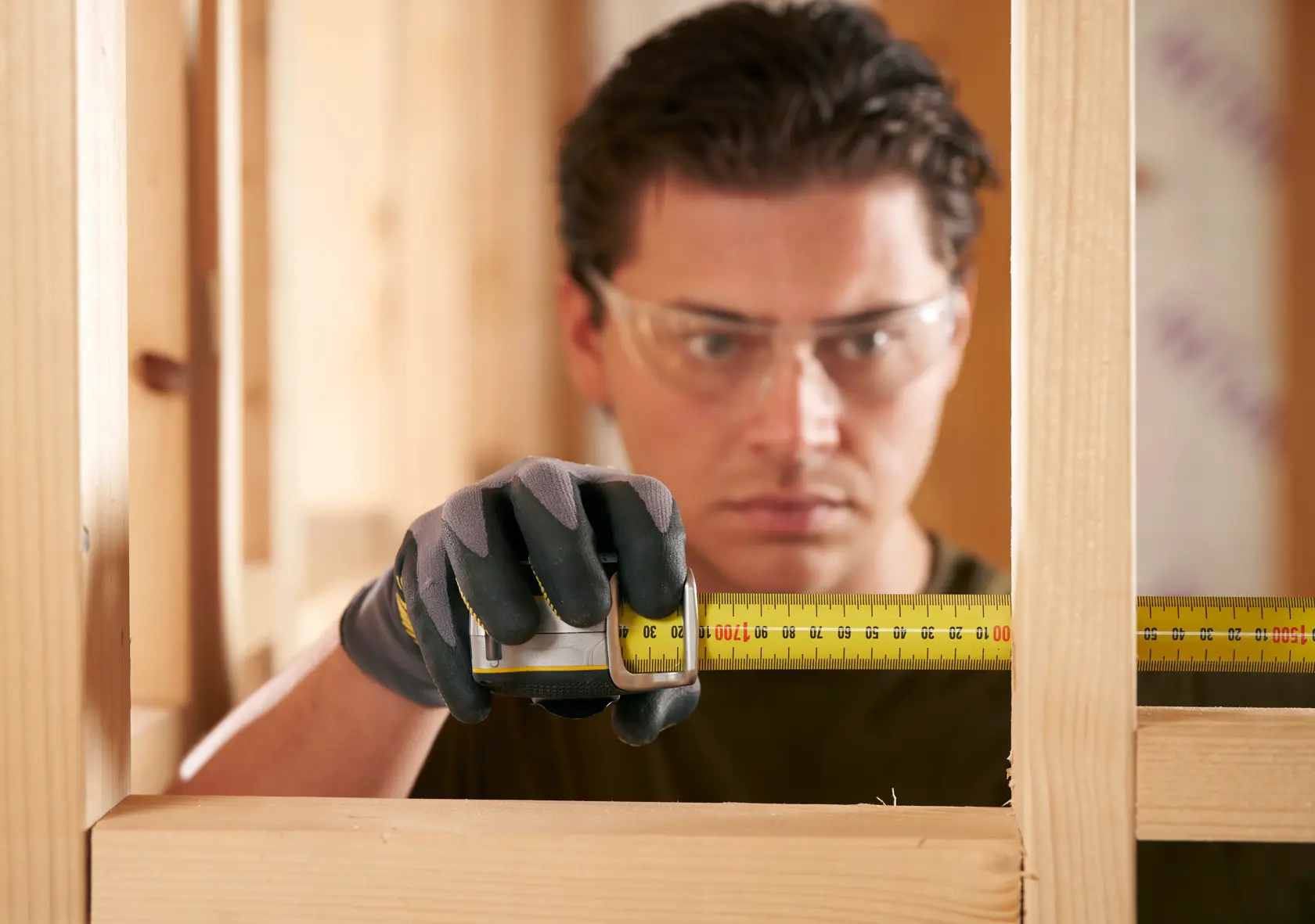 STANLEY FMHT38219-3 tape measure in use, person wearing work gloves measuring wooden frame, close-up photography.