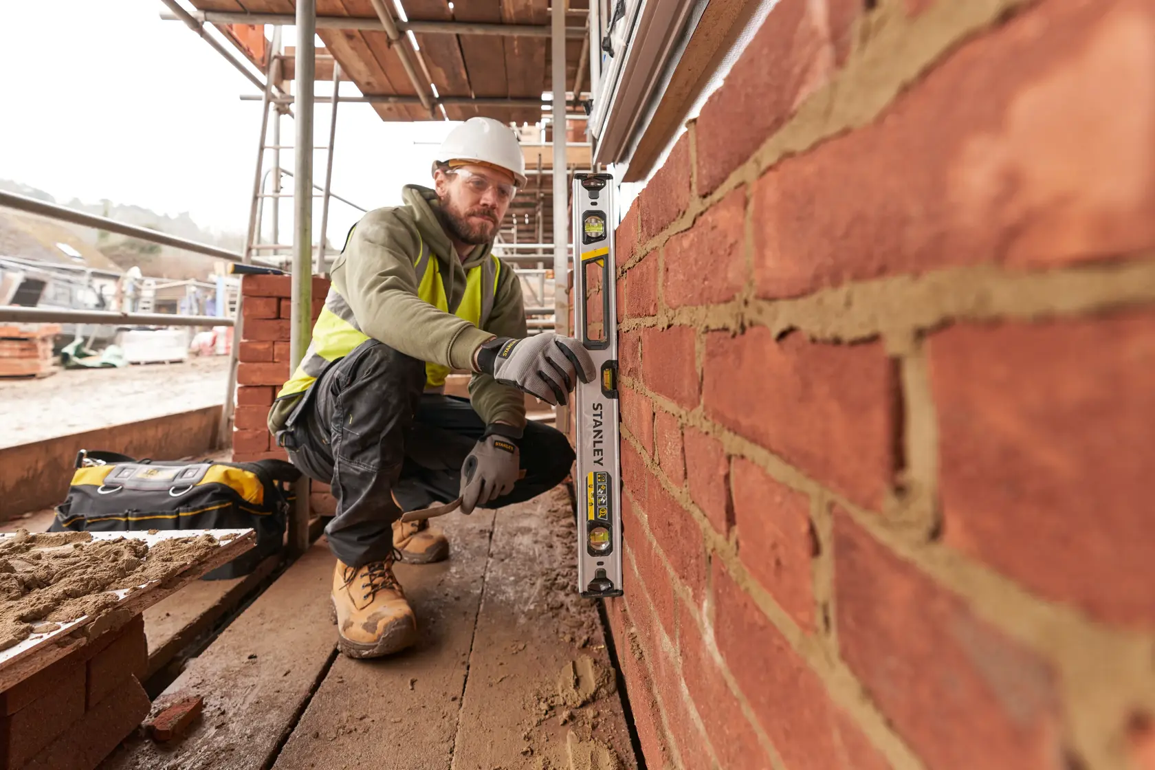 Photo of STANLEY FMHT43673-1 spirit level used by worker checking alignment on brick wall at construction site.