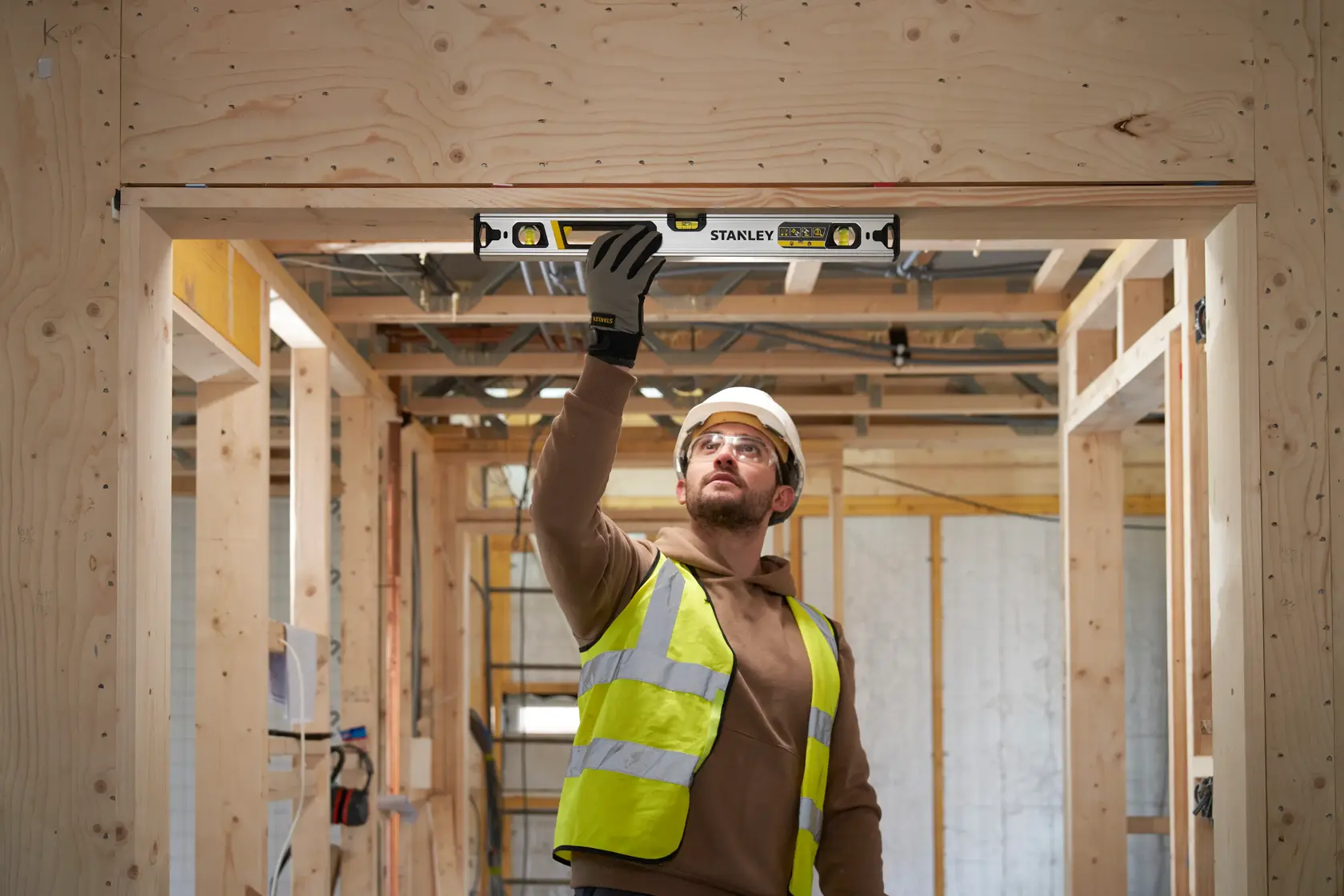 Worker uses STANLEY FMHT43673-1 spirit level in wooden doorway frame on construction site.