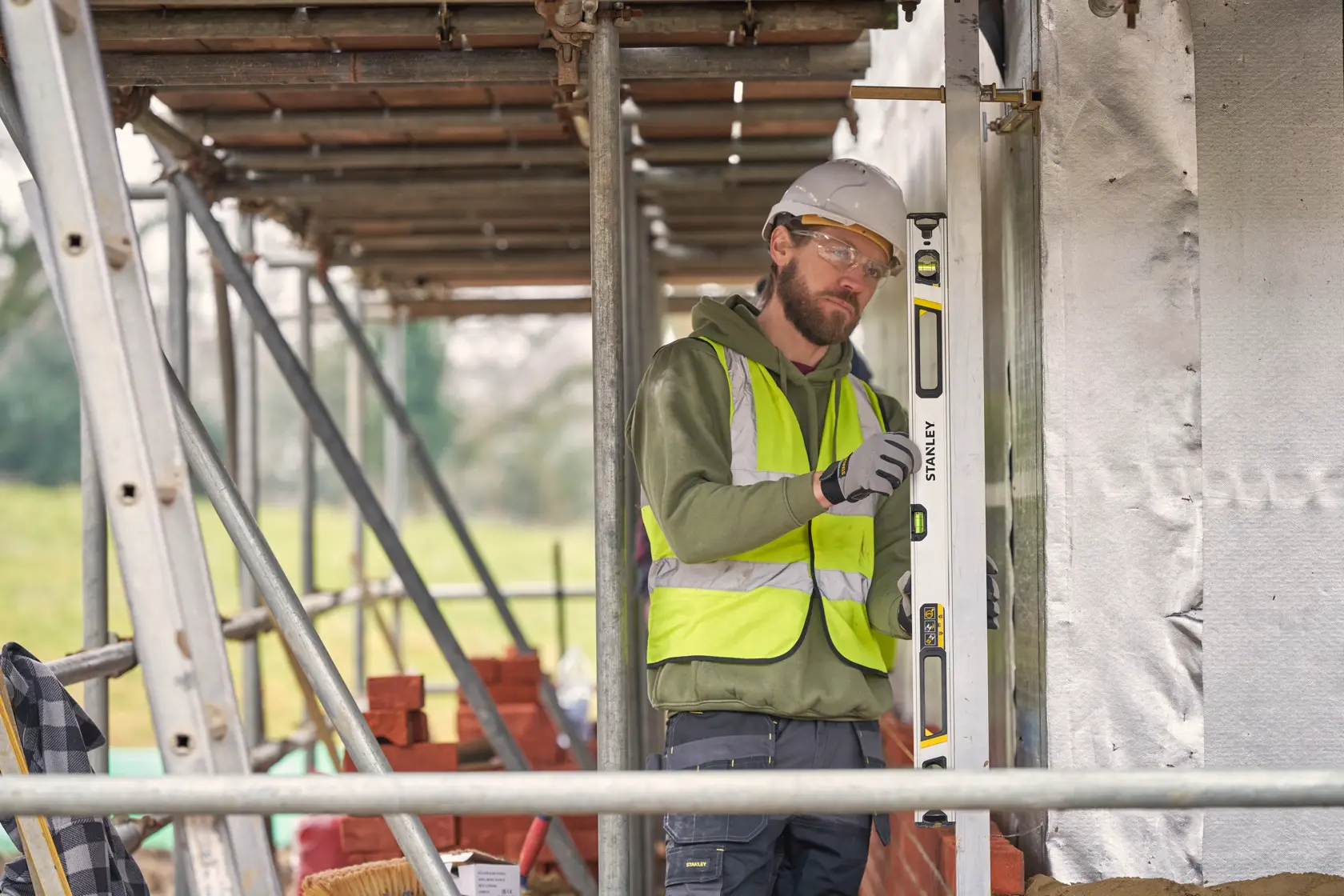 Photo of worker using STANLEY FMHT43674-1 spirit level at construction site, wearing safety vest and helmet.