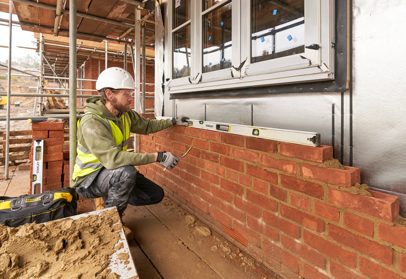 STANLEY FMHT43678-1 spirit level used by a worker checking horizontal alignment on a brick wall, side view.