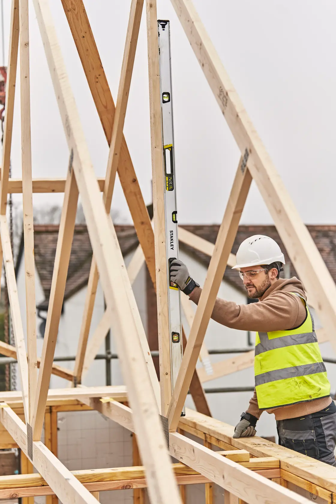 STANLEY FMHT43678-1 spirit level used vertically by worker in safety gear on wood framing at construction site.