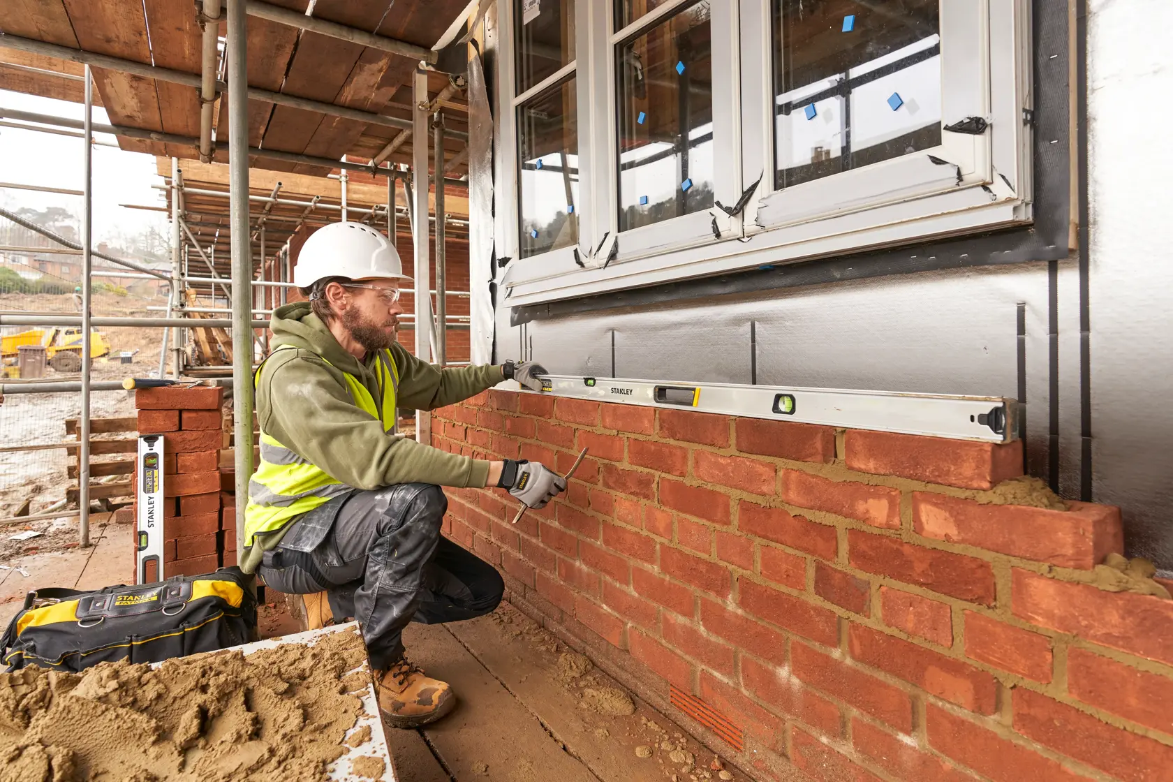 STANLEY FMHT43679-1 spirit level used by a builder on a brick wall at a construction site, side angle.