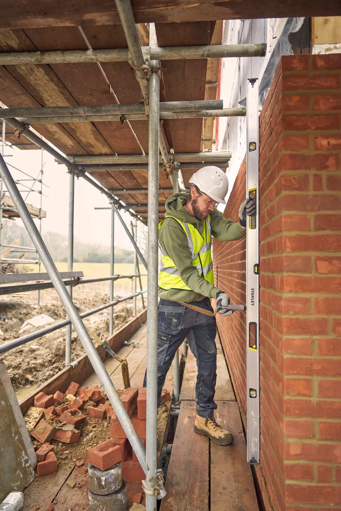 STANLEY FMHT43679-1 spirit level in use by a construction worker checking a brick wall on scaffolding.