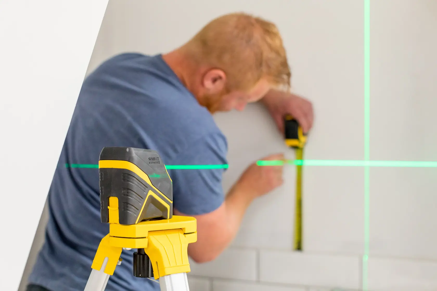 STANLEY FMHT77586-1 laser level on tripod projecting green lines, person measuring wall.