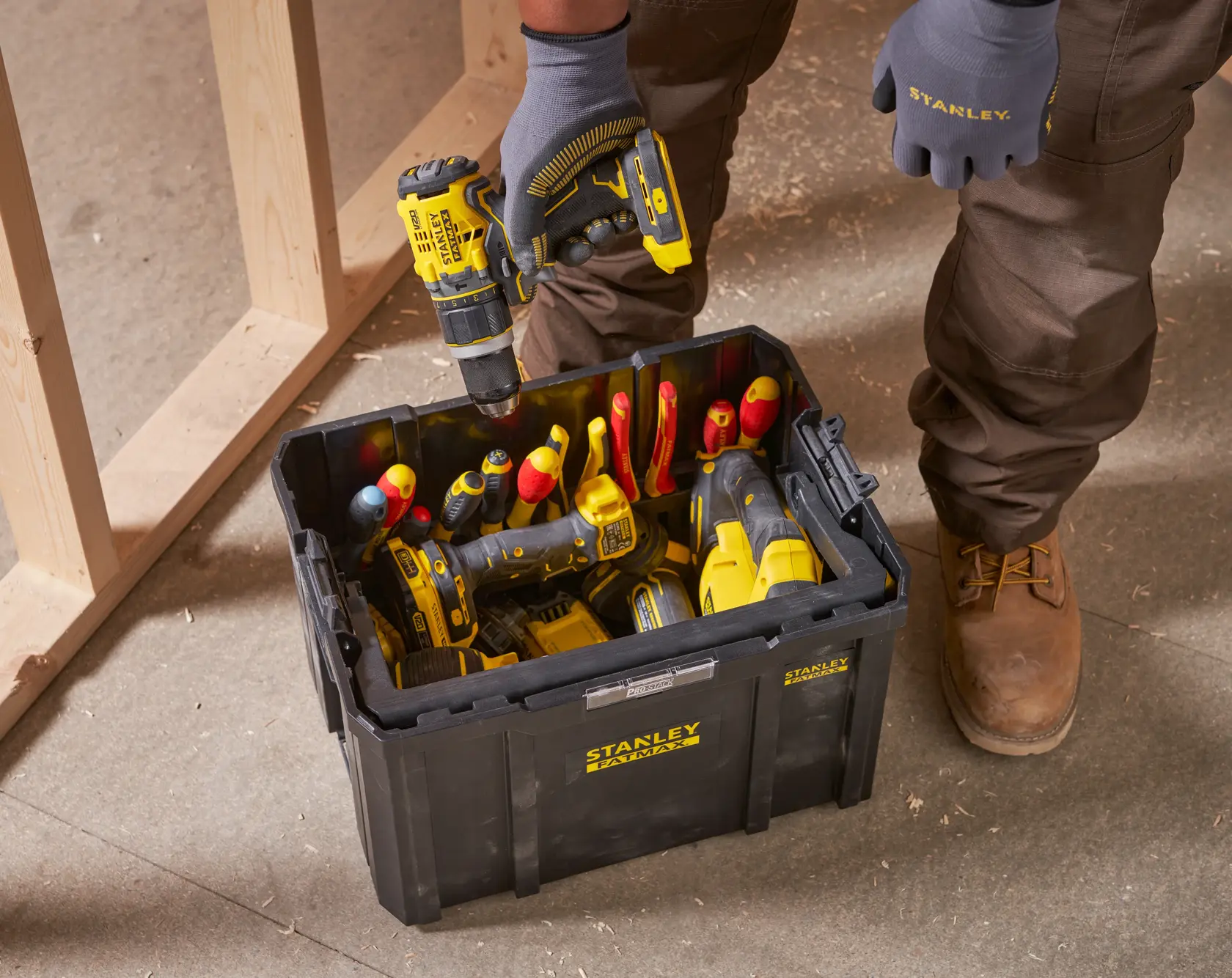 STANLEY FMST1-75794 black toolbox on jobsite floor, filled with hand tools and power tools, person holding drill.