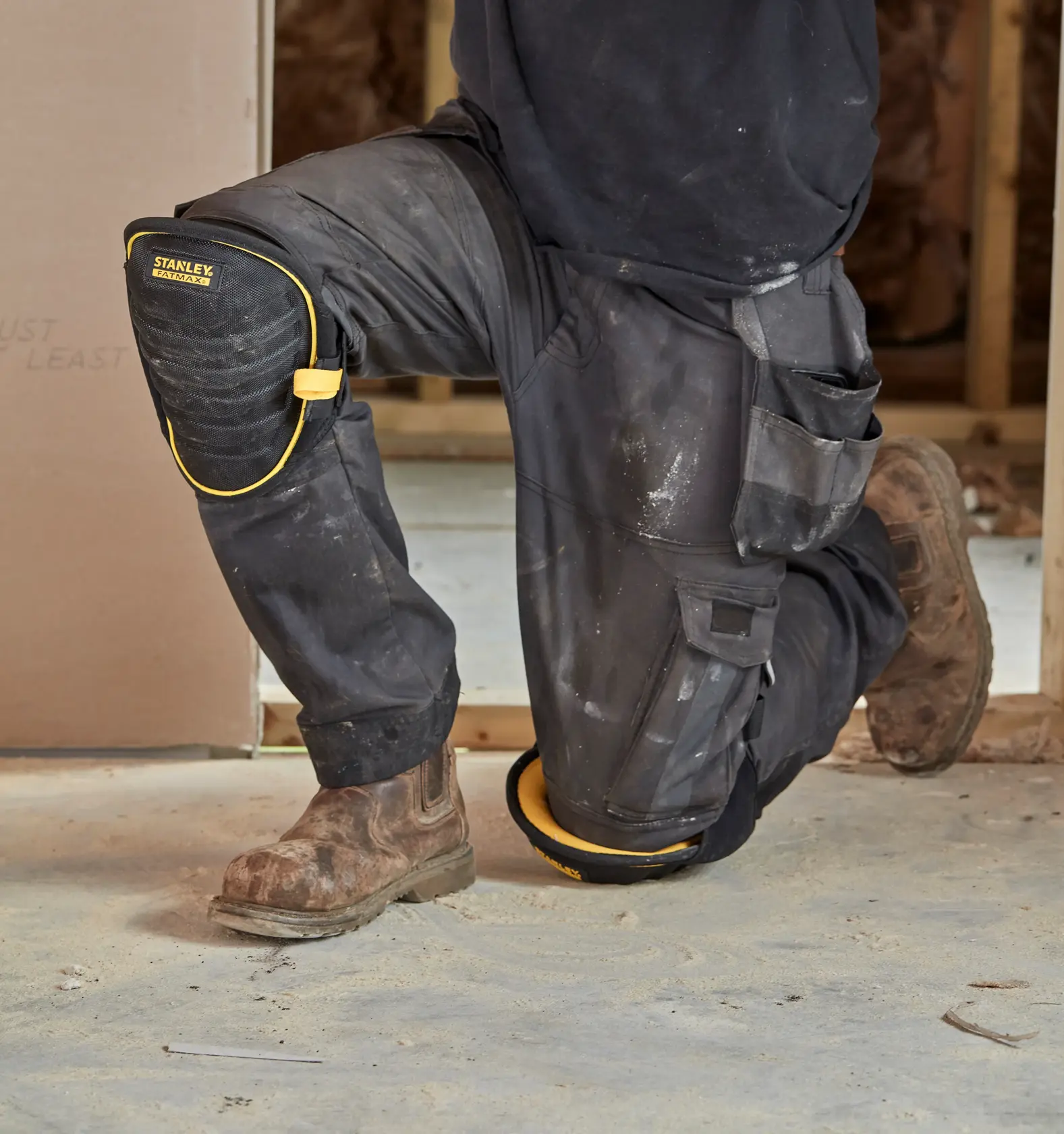 STANLEY FMST82959-1 black and yellow knee pad worn by a person kneeling on a construction site.