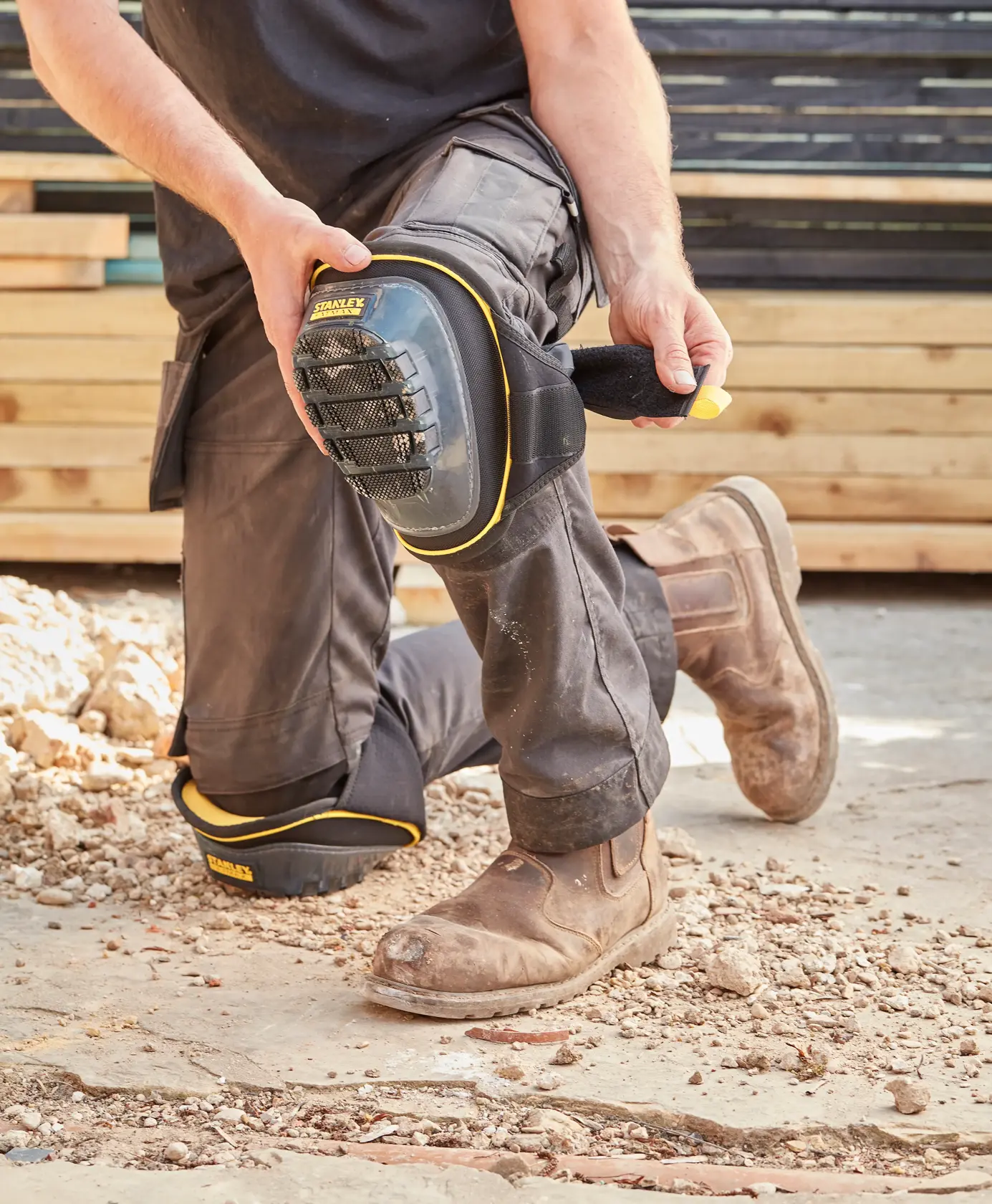 STANLEY FMST82960-1 knee pad with black and yellow trim being strapped on by worker outdoors.