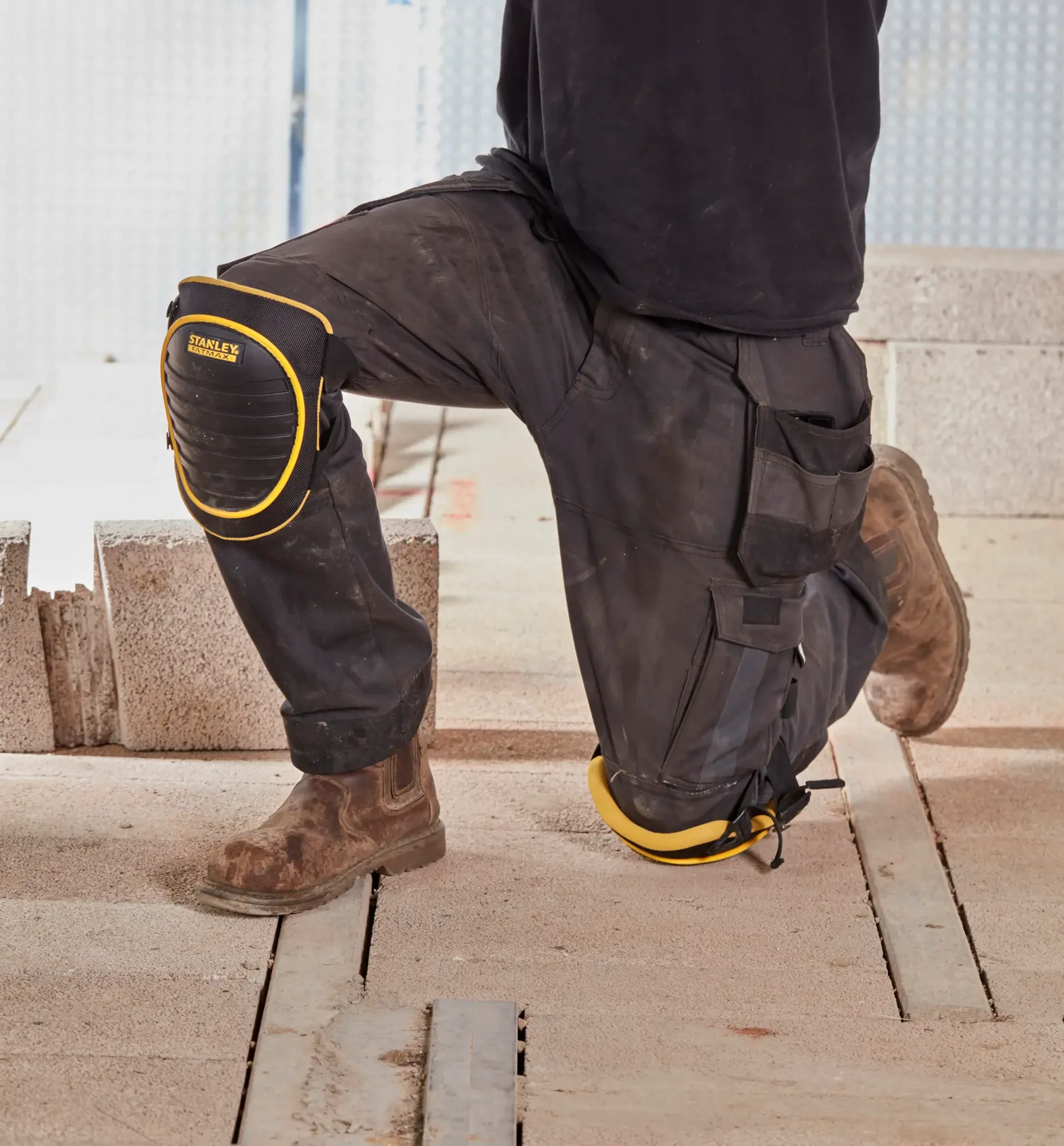 STANLEY FMST82961-1 knee pads worn on work pants at a construction site, black with yellow trim.