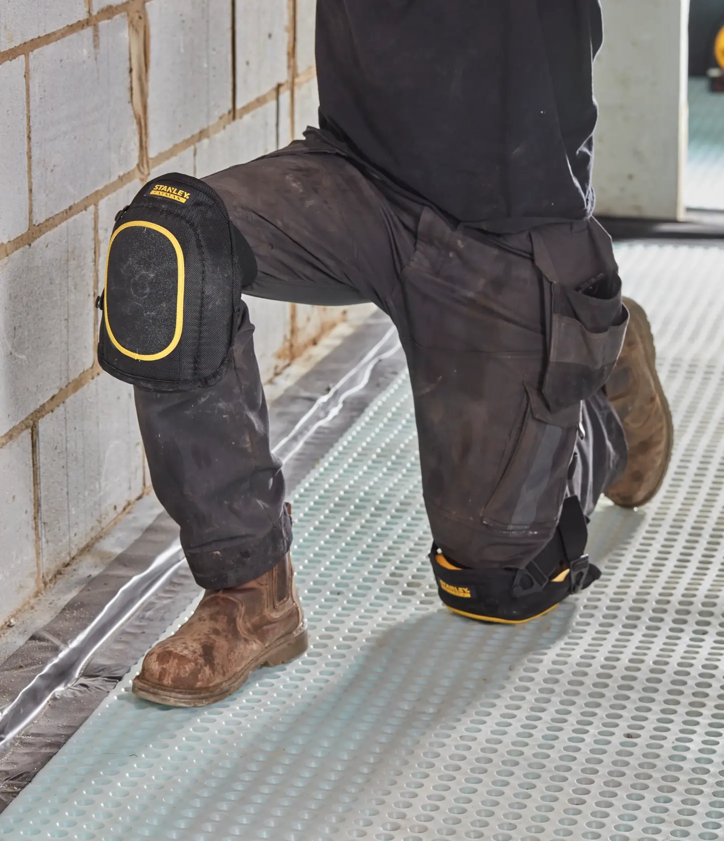 STANLEY FMST82962-1 knee pads, black with yellow trim, worn by worker kneeling on construction site.