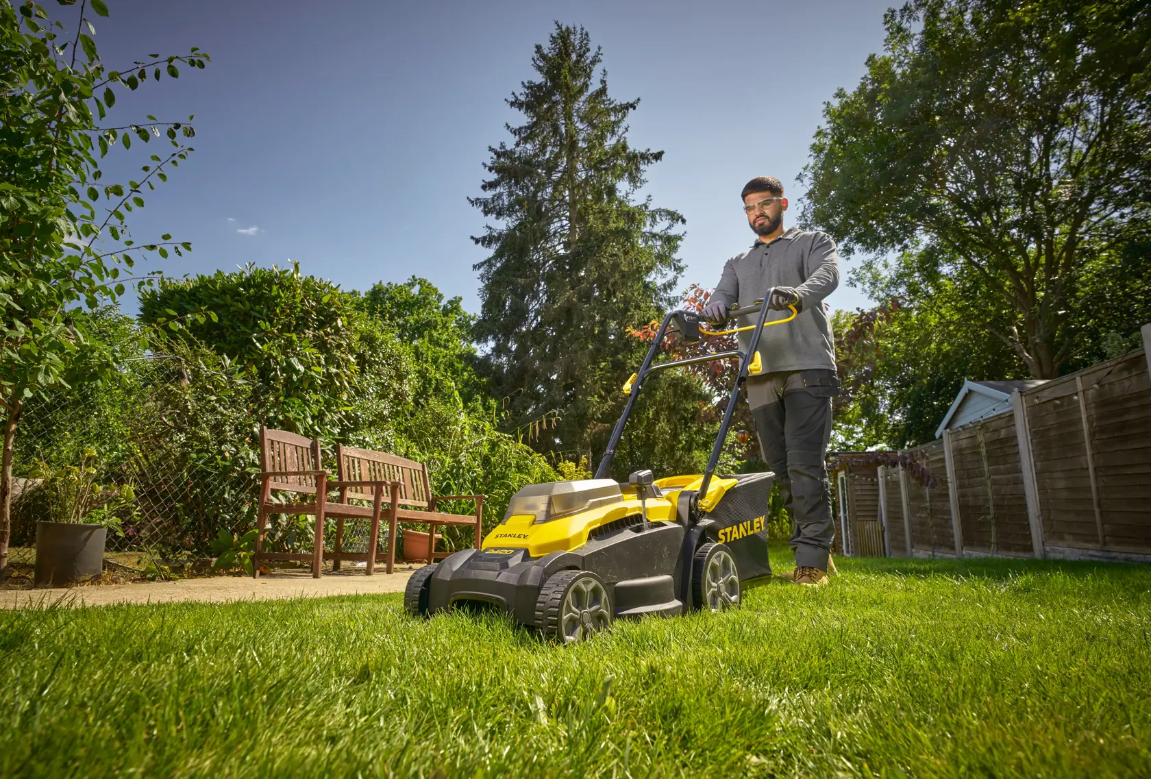STANLEY SCMWP3701N lawn mower in use on grass in a garden, person pushing mower, photographed outdoors.