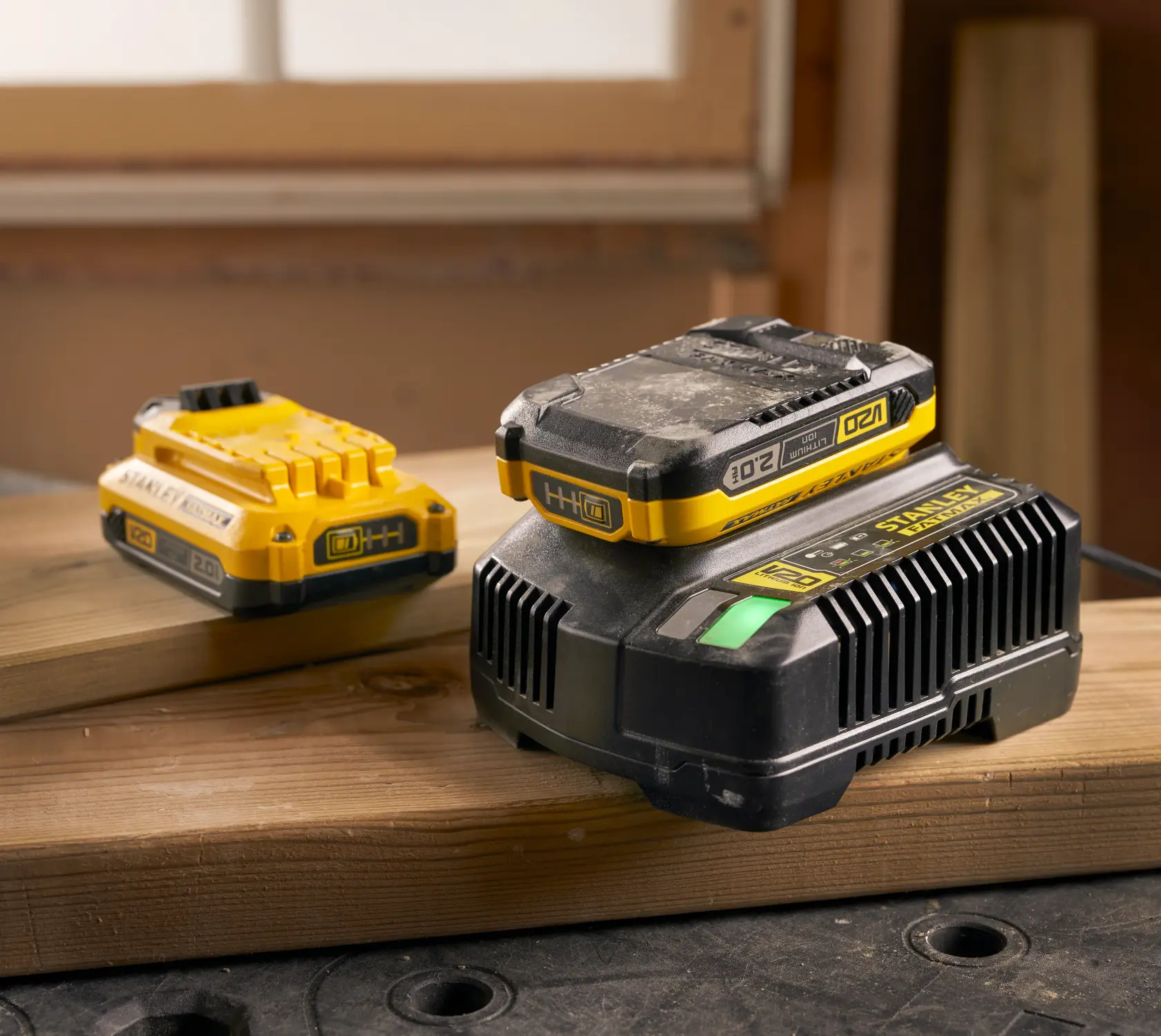 Photo of STANLEY SFMCB12D2 yellow 20V battery and charger set on wooden planks in workshop.