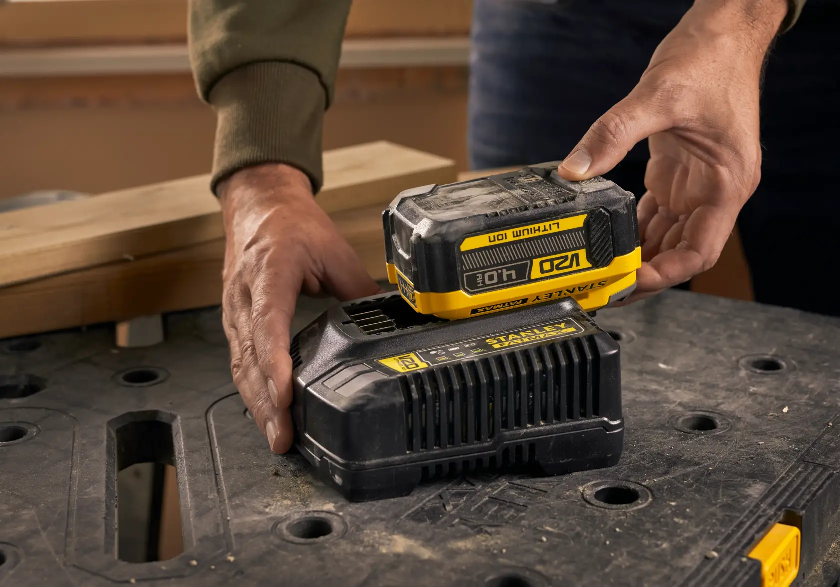 Photo of STANLEY SFMCB14M1 18V lithium-ion battery being placed on charger, shown on a workbench.