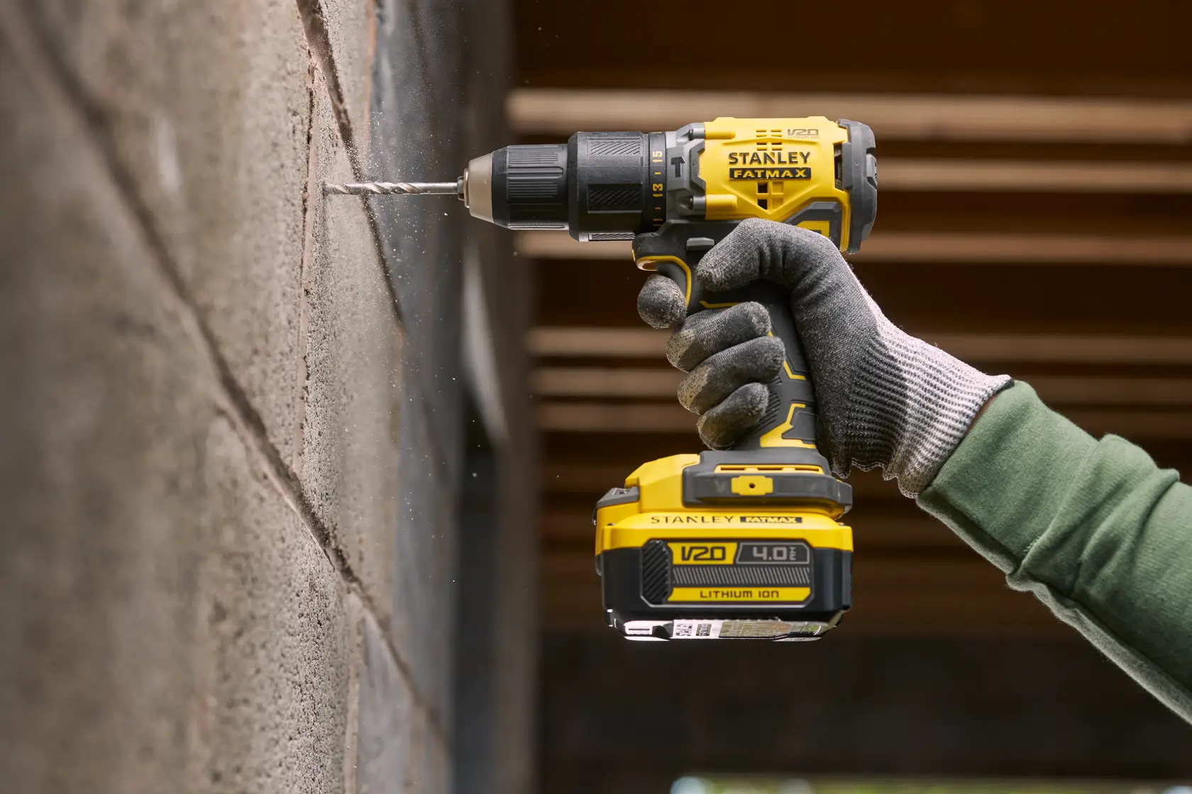 STANLEY SFMCB14M1 cordless drill in use, drilling into concrete wall, close-up view of tool and gloved hand.