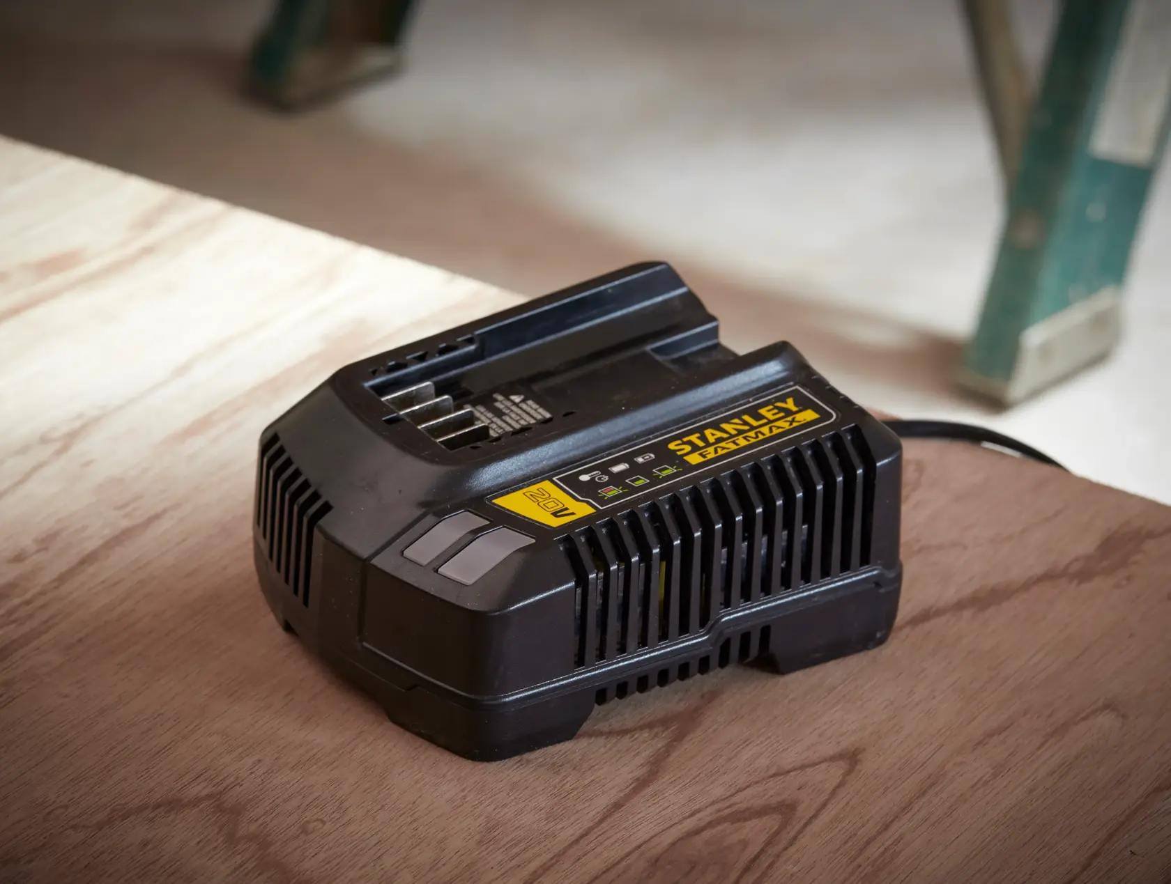 Photo of STANLEY SFMCB14 black battery charger on wooden surface, labeled FATMAX, shown in workshop setting.