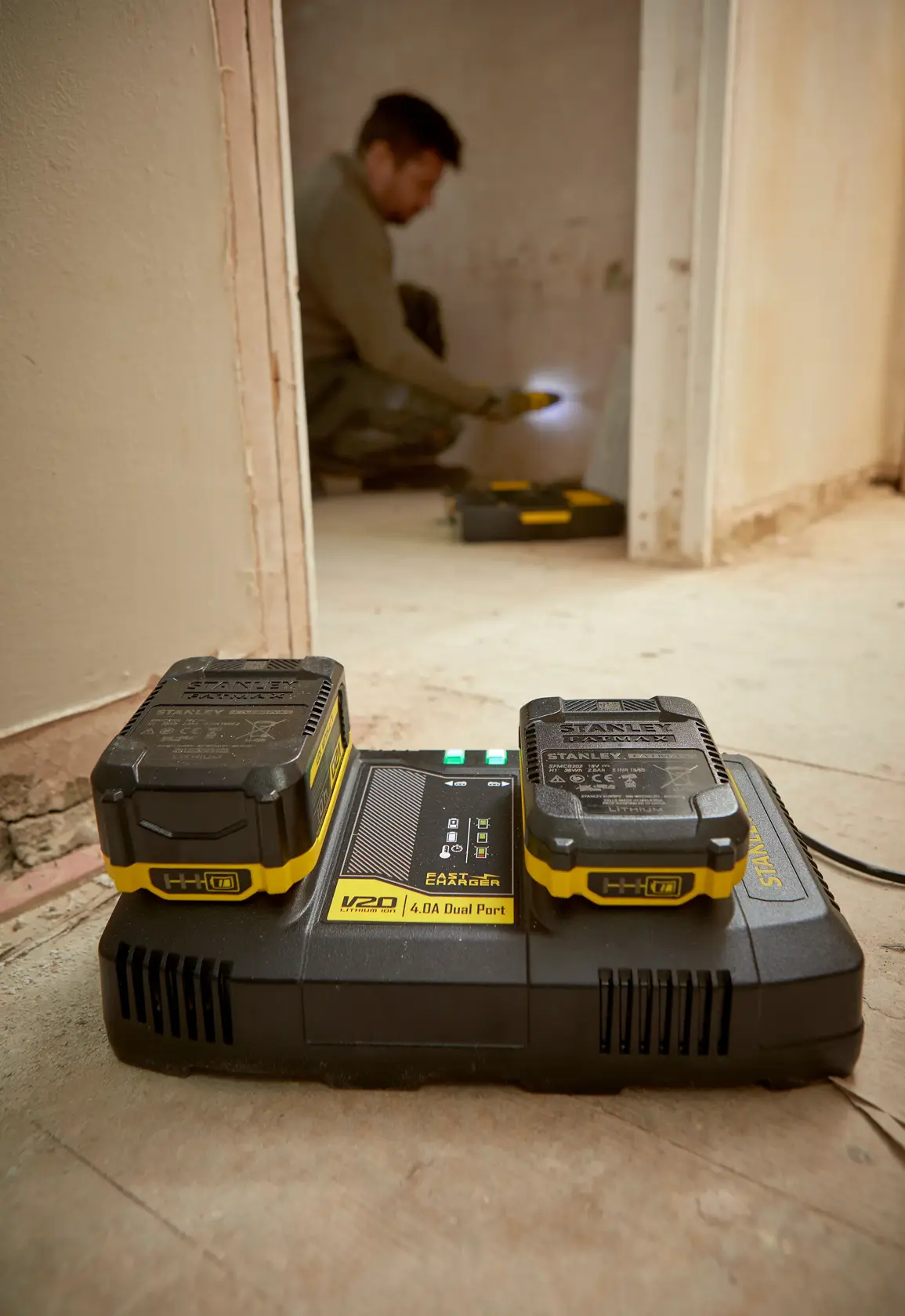 STANLEY SFMCB24 dual port charger with two V20 batteries on a floor in a construction setting.