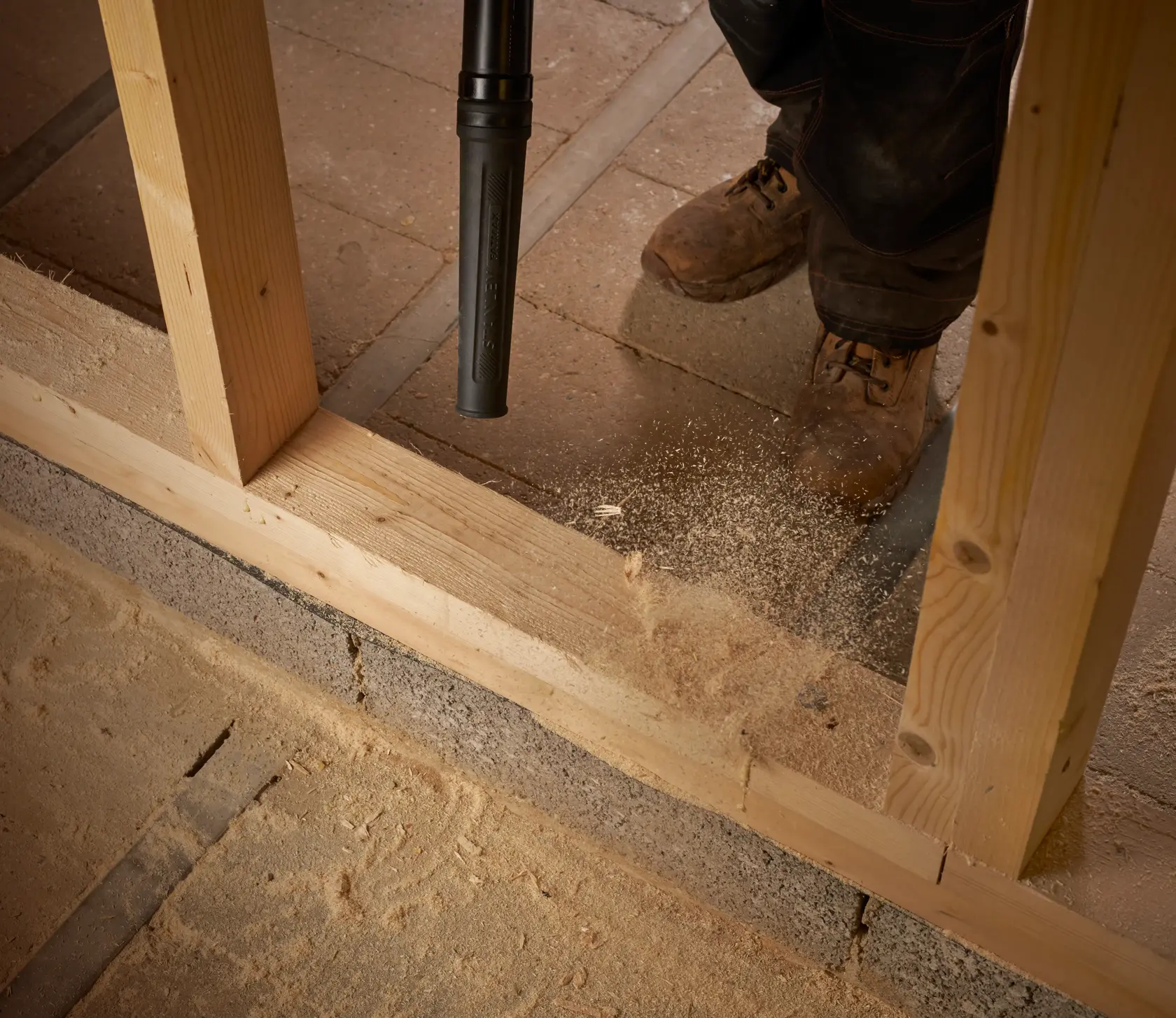 STANLEY SFMCBL01B blower cleaning sawdust on floor at construction site, close-up of nozzle and work boots.
